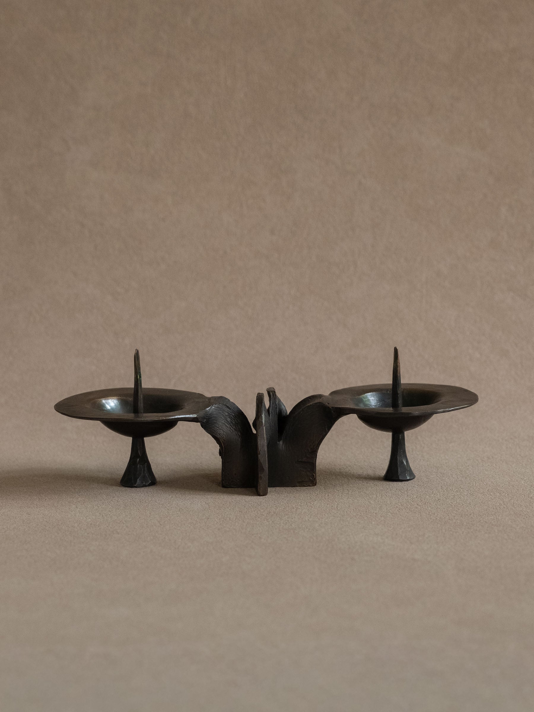 Front view of the low two-light bronze candleholder with symmetrical candle plates and central sculptural support.