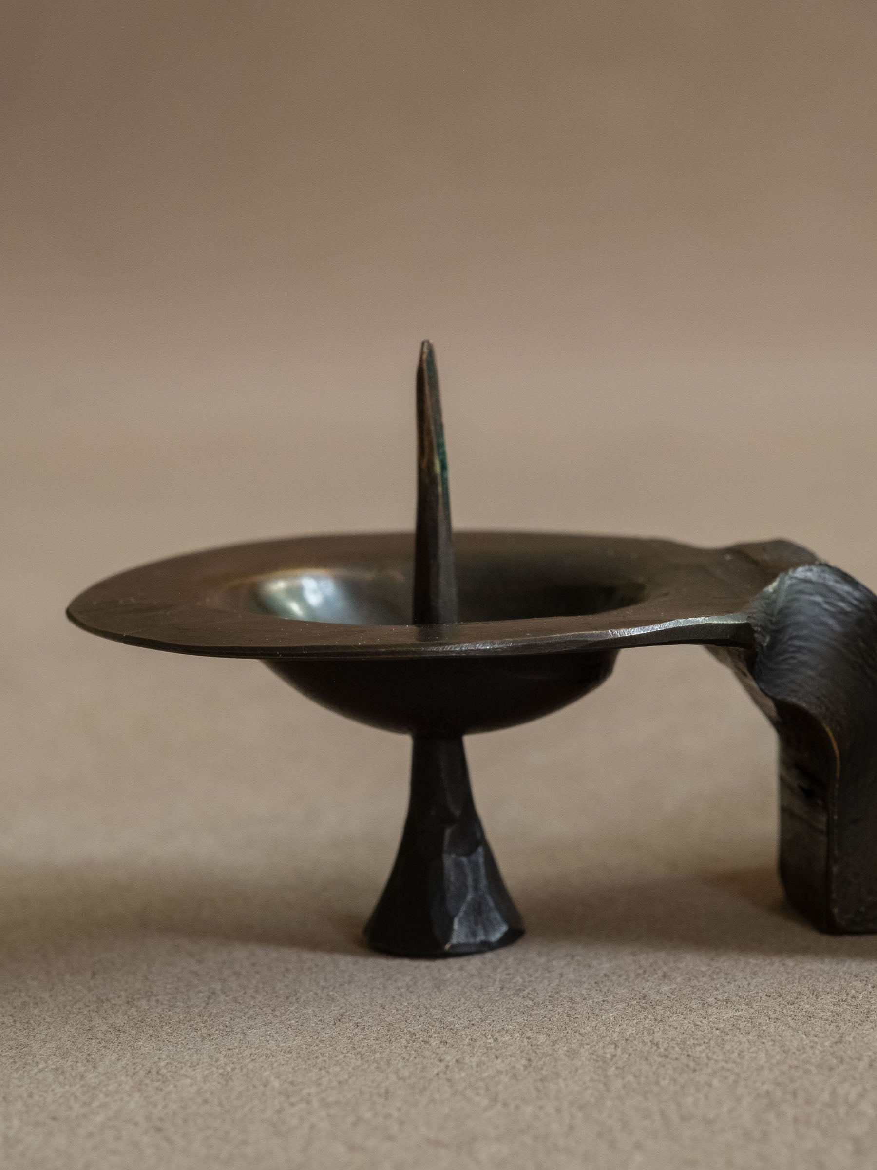 Close view of one bronze candle plate and spike, with the textured tapered foot below.