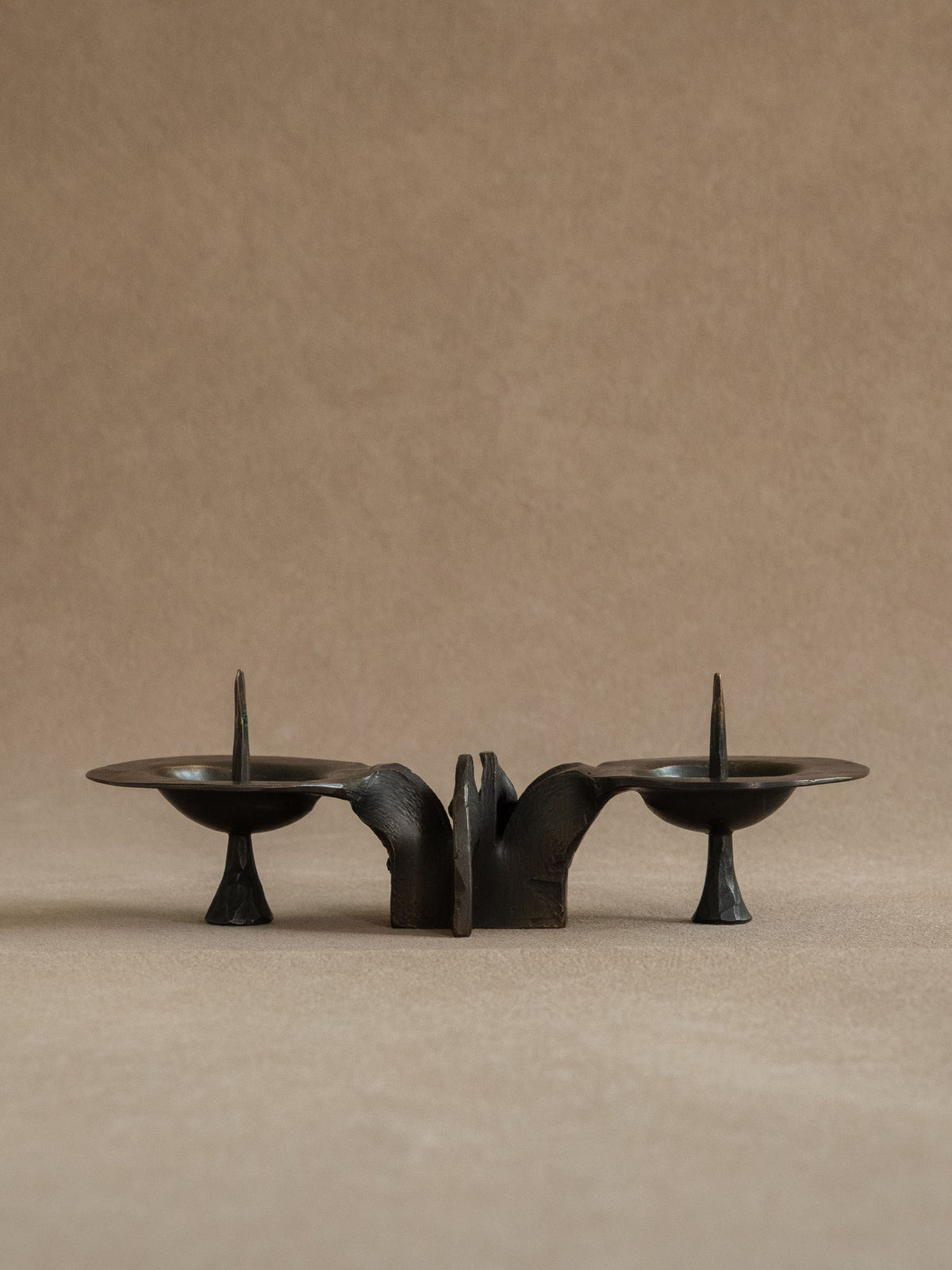 Full front hero view of the attributed Bergmeister two-light bronze candleholder against a warm neutral background.
