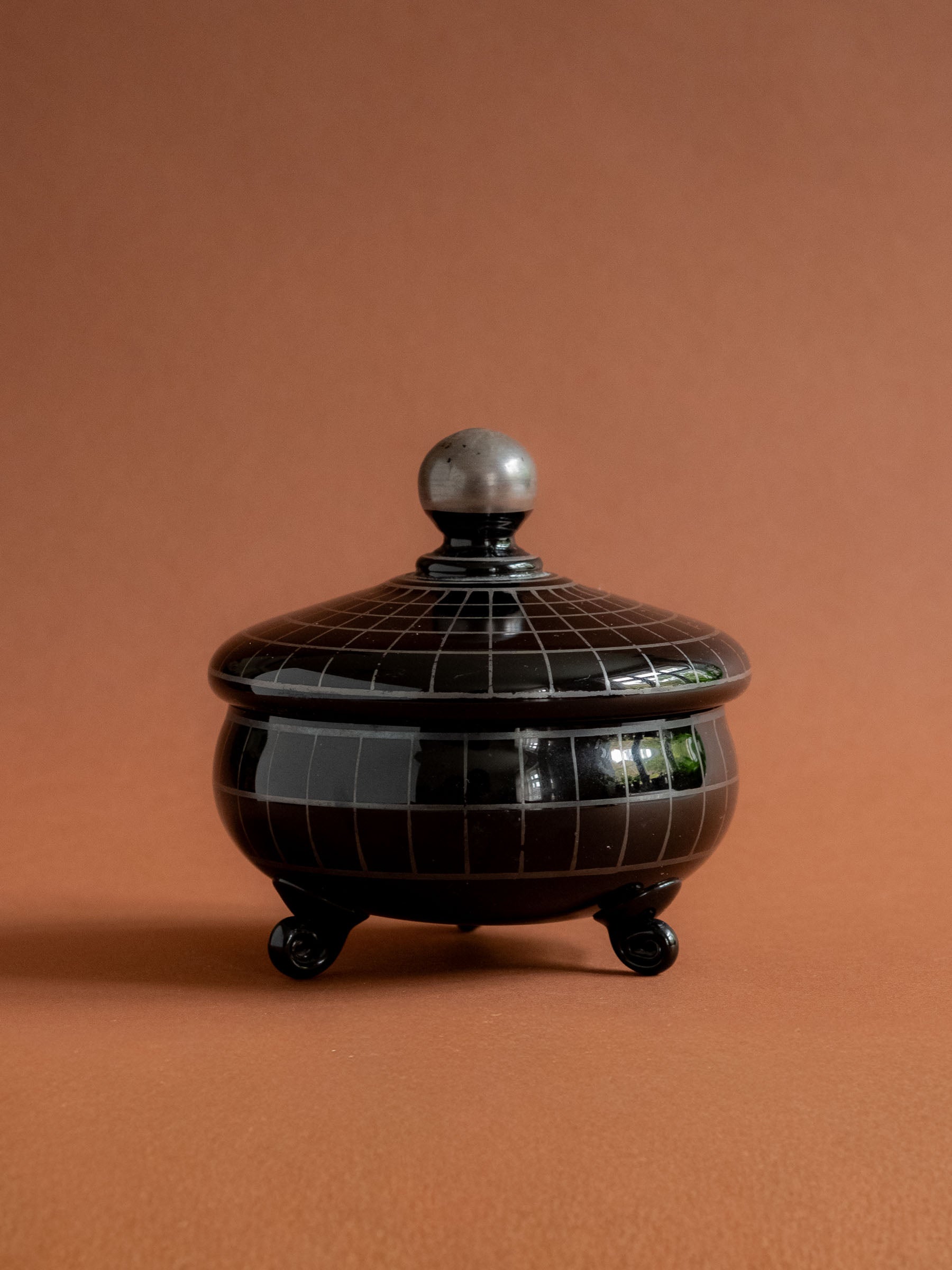 Full hero view of the closed black Hyalith glass Art Deco box against a warm reddish background.