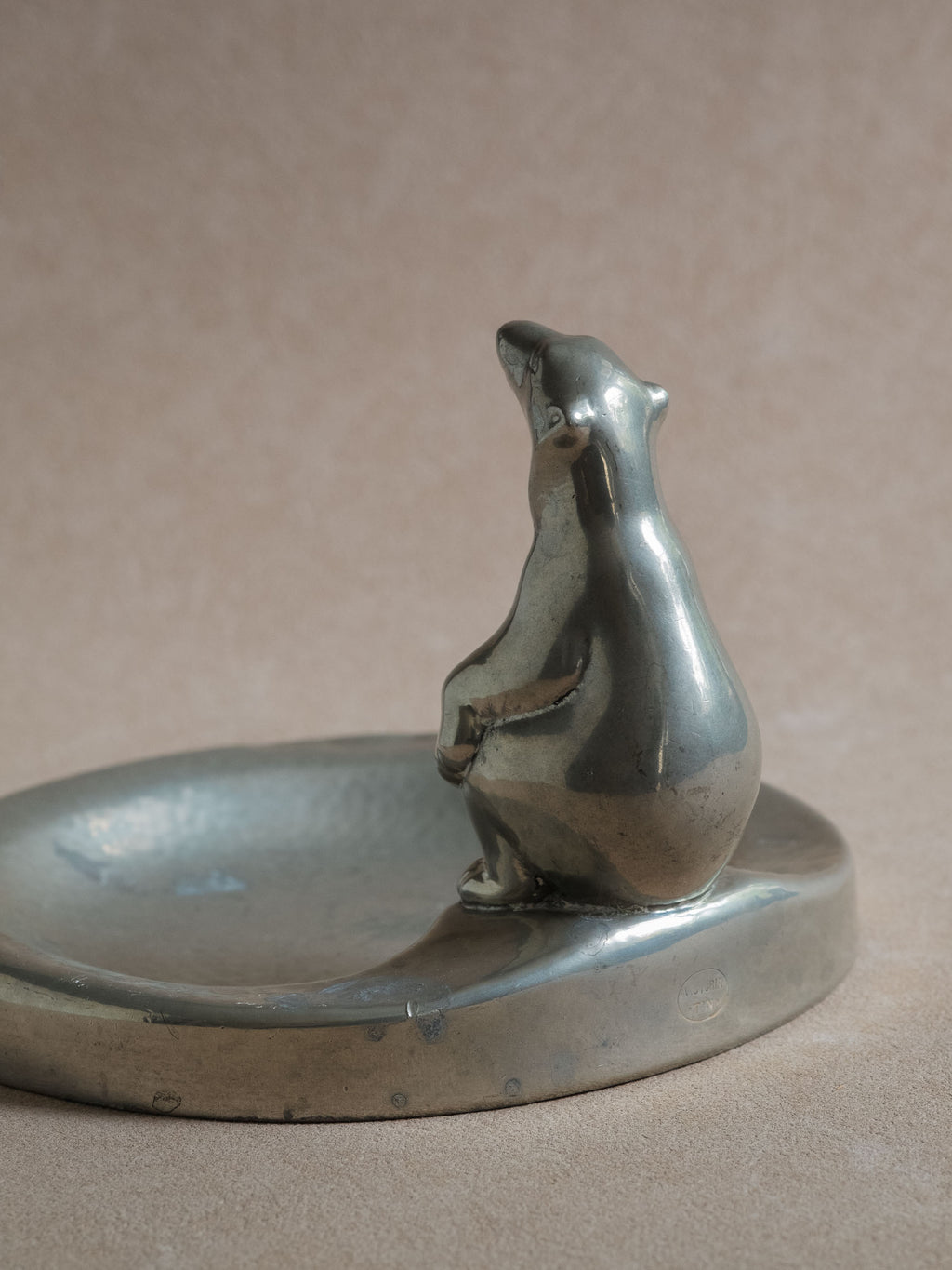 Side view of a pewter polar bear figural dish, with the bear figure positioned at the edge of the shallow bowl.
