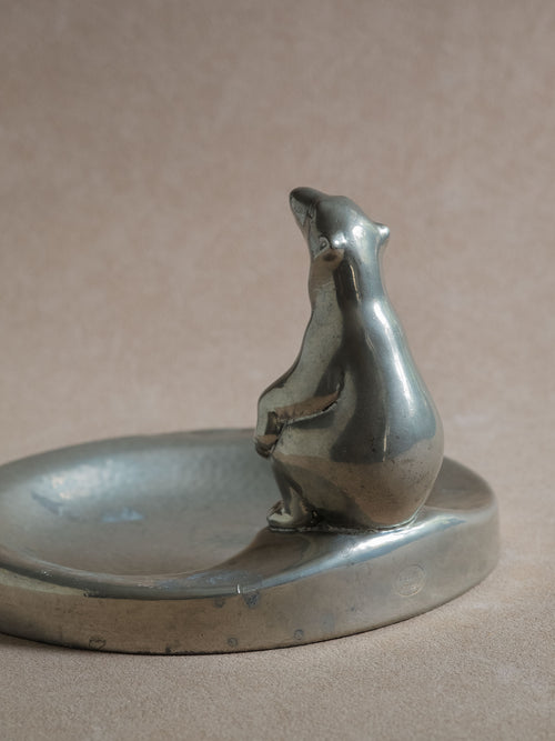 Side view of a pewter polar bear figural dish, with the bear figure positioned at the edge of the shallow bowl.

