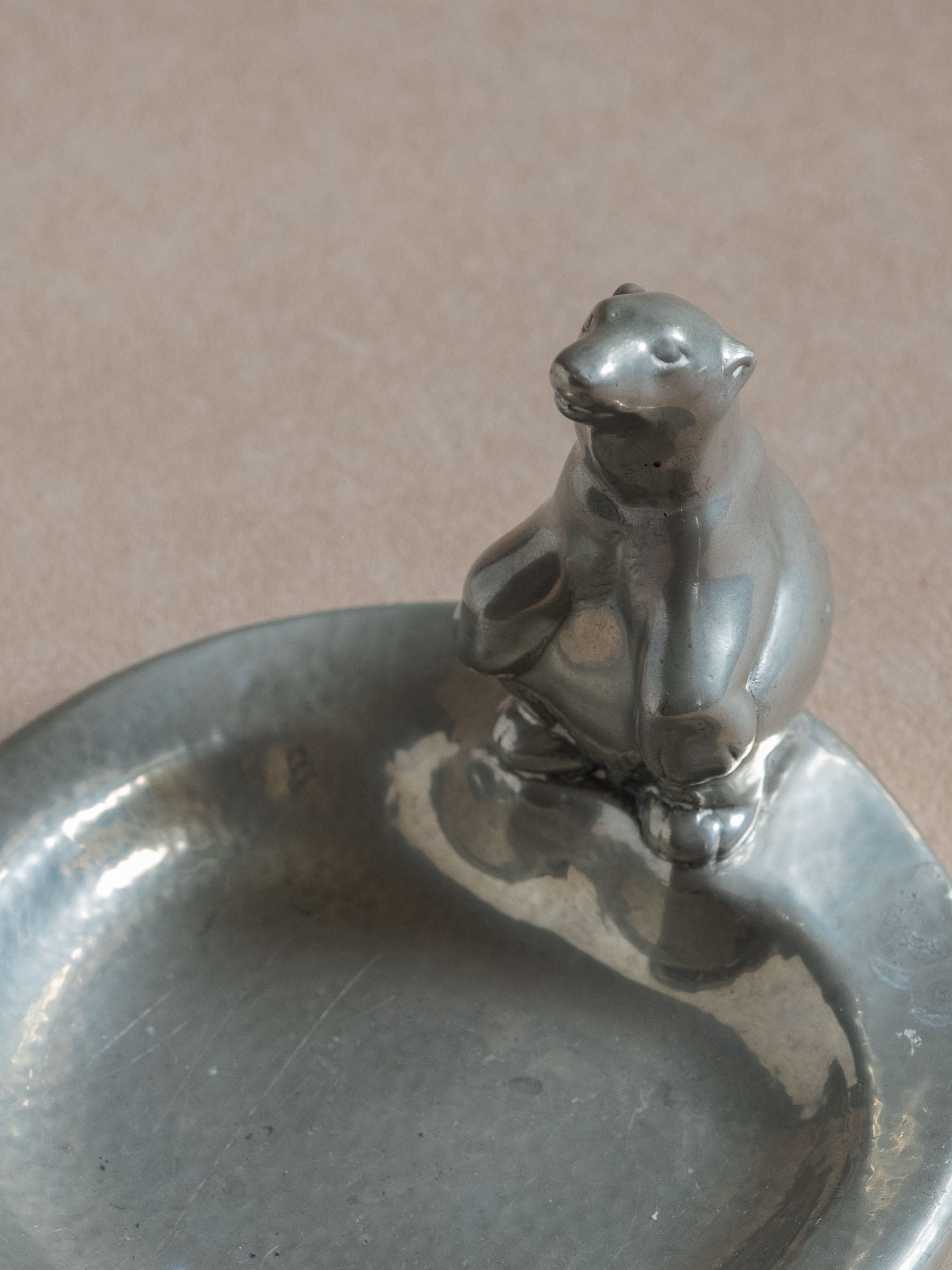 Close-up of the polar bear figure on a pewter dish, showing the simplified animal form and surface wear inside the bowl.