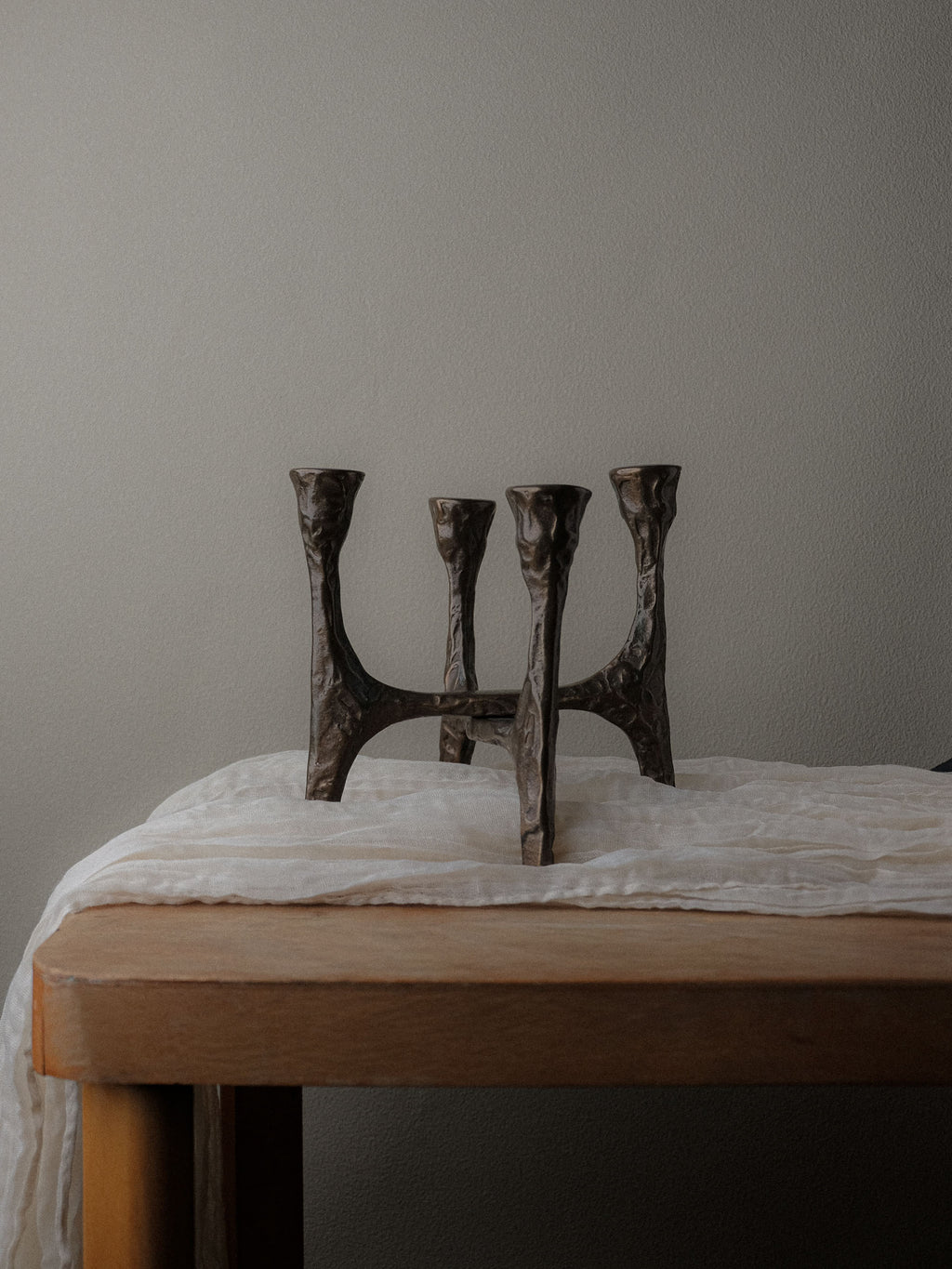 Brutalist four-arm bronze candleholder, Germany, 1970s, placed on a wooden table against a neutral wall.