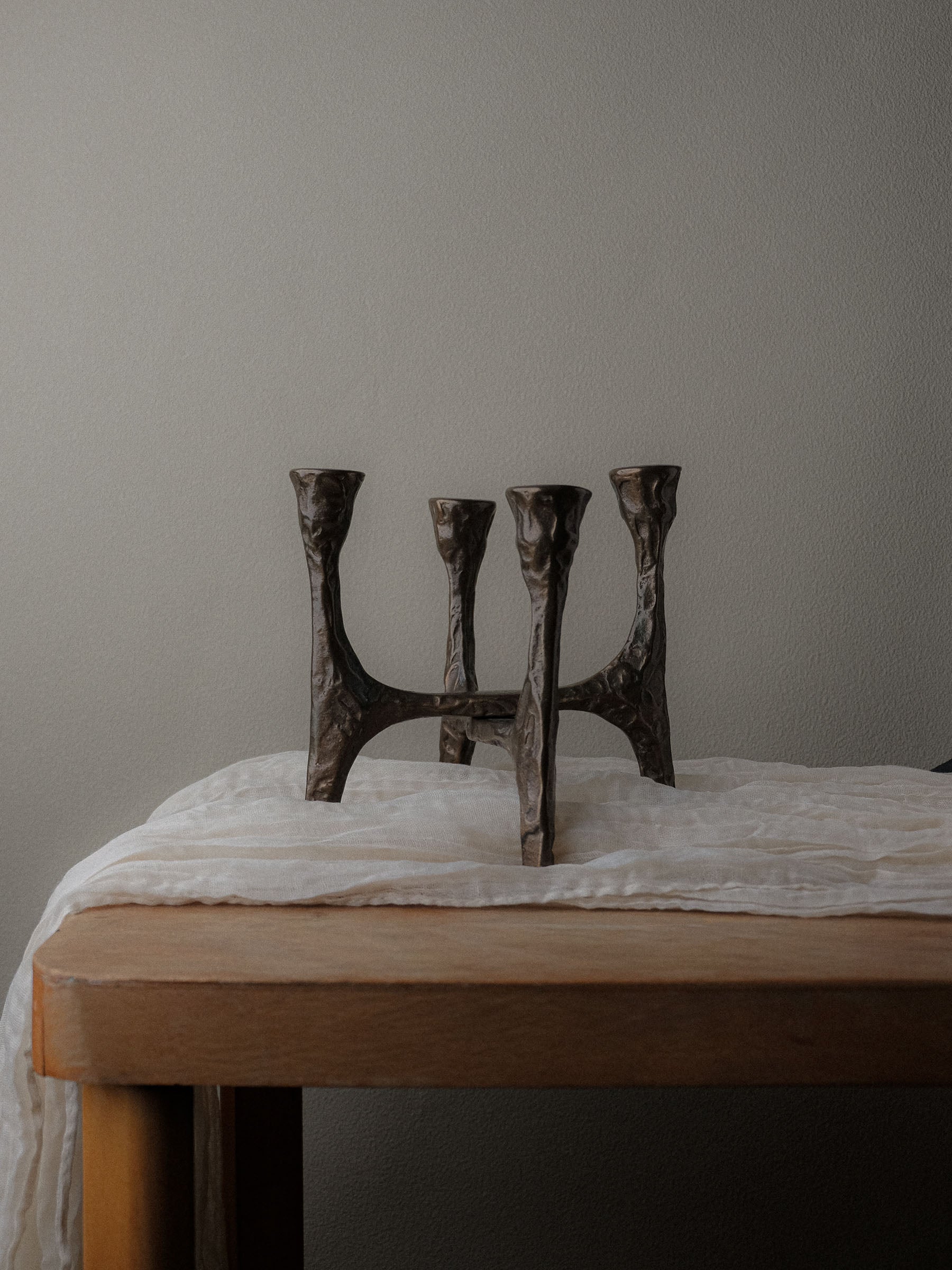 Brutalist four-arm bronze candleholder, Germany, 1970s, placed on a wooden table against a neutral wall.