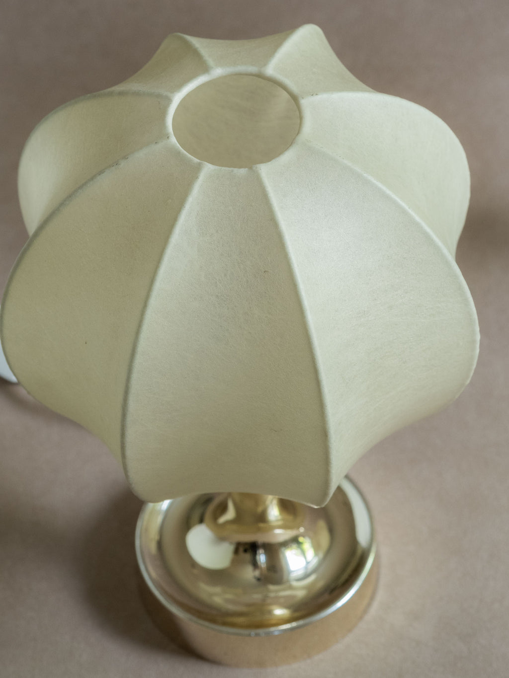 Close detail of a Goldkant Salbo cocoon table lamp base showing the reflective chrome-effect finish, stem, and surface wear.

