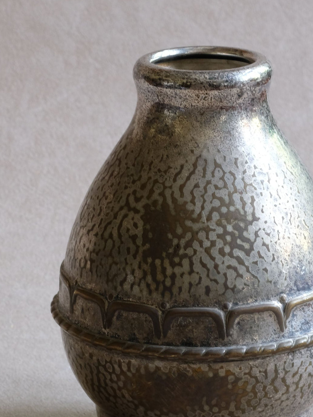 Detail of the HAGS vase showing worn silver plating revealing warmer yellow base metal, hammered texture and raised decoration.