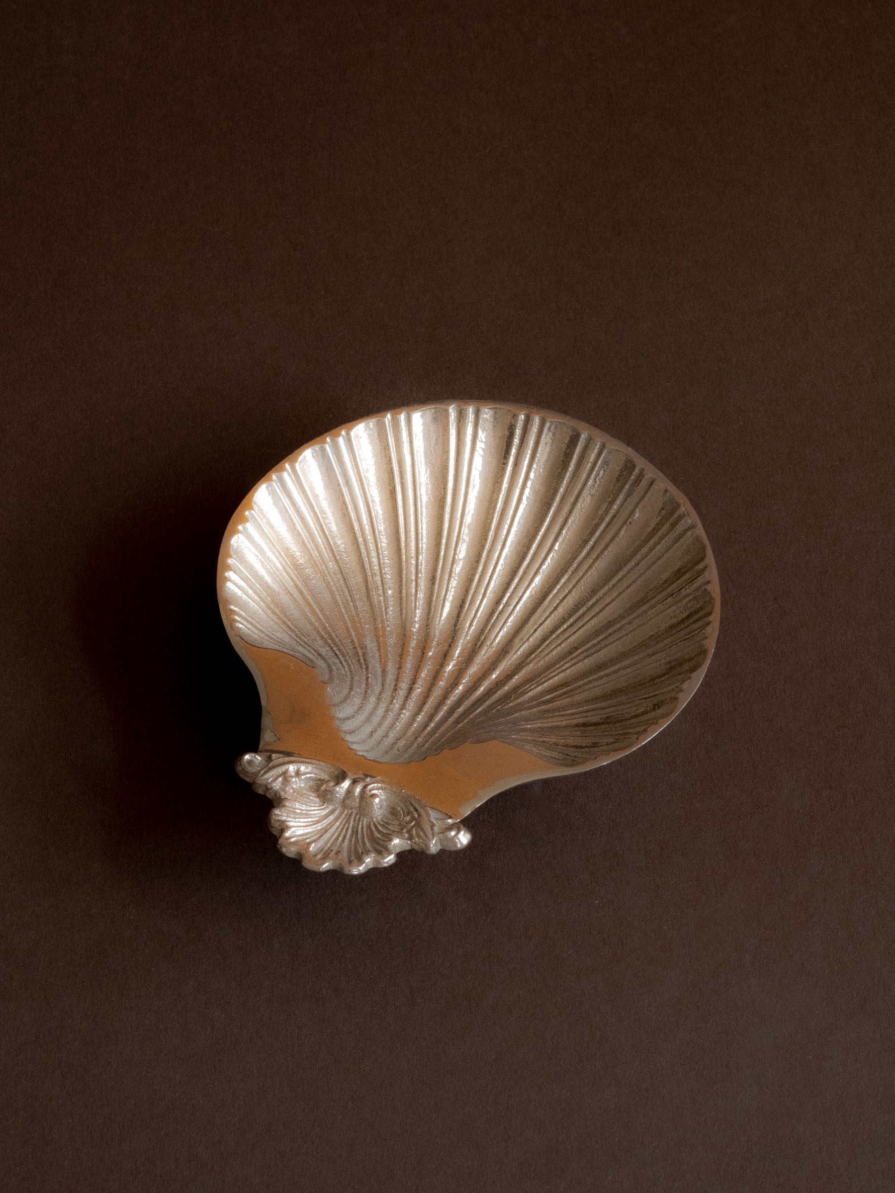 Angel view of the Hans Baier silver-plated scallop shell dish on a brown background, showing the back of the shell form and the small shell motif at the top.