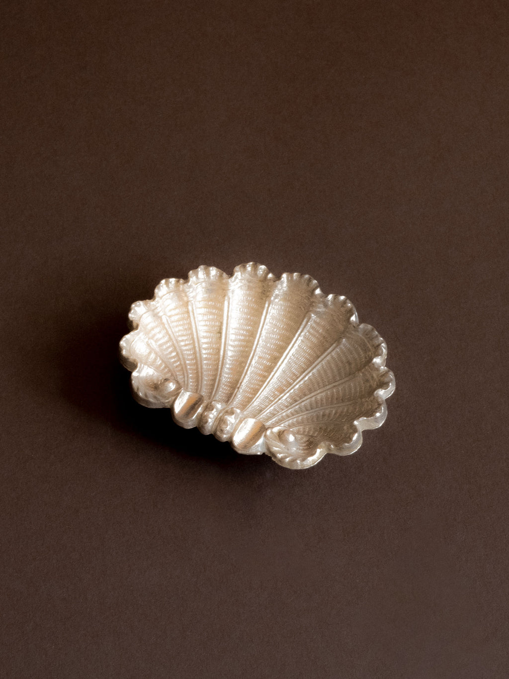 Angel view of a small silver-plated shell ashtray photographed on a brown background.