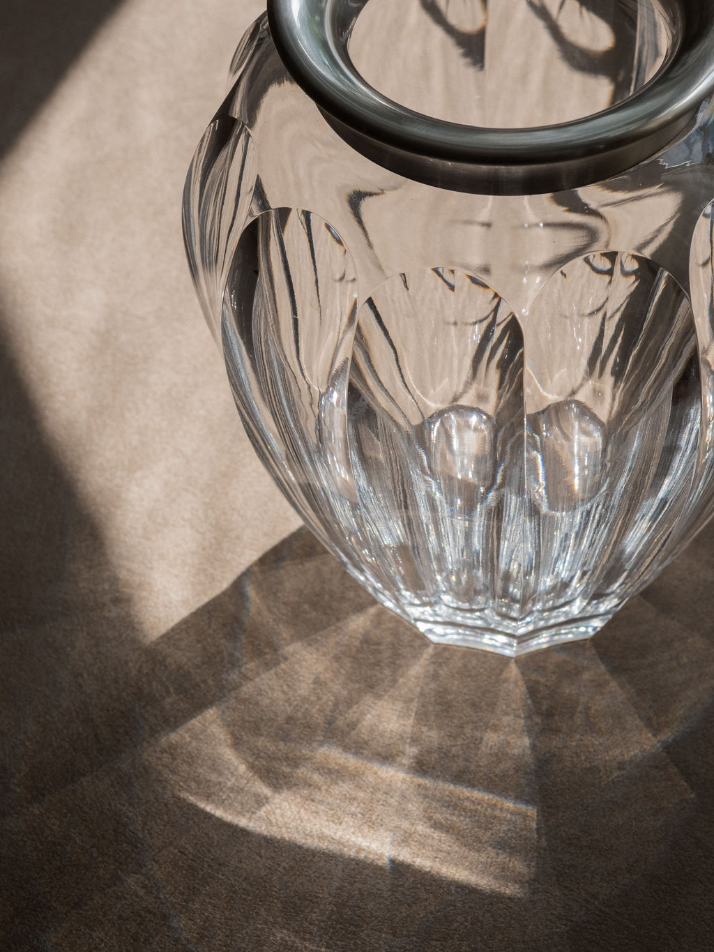 Top detail of the crystal vase showing the sterling silver rim, cut glass body and refracted light on the surface below.