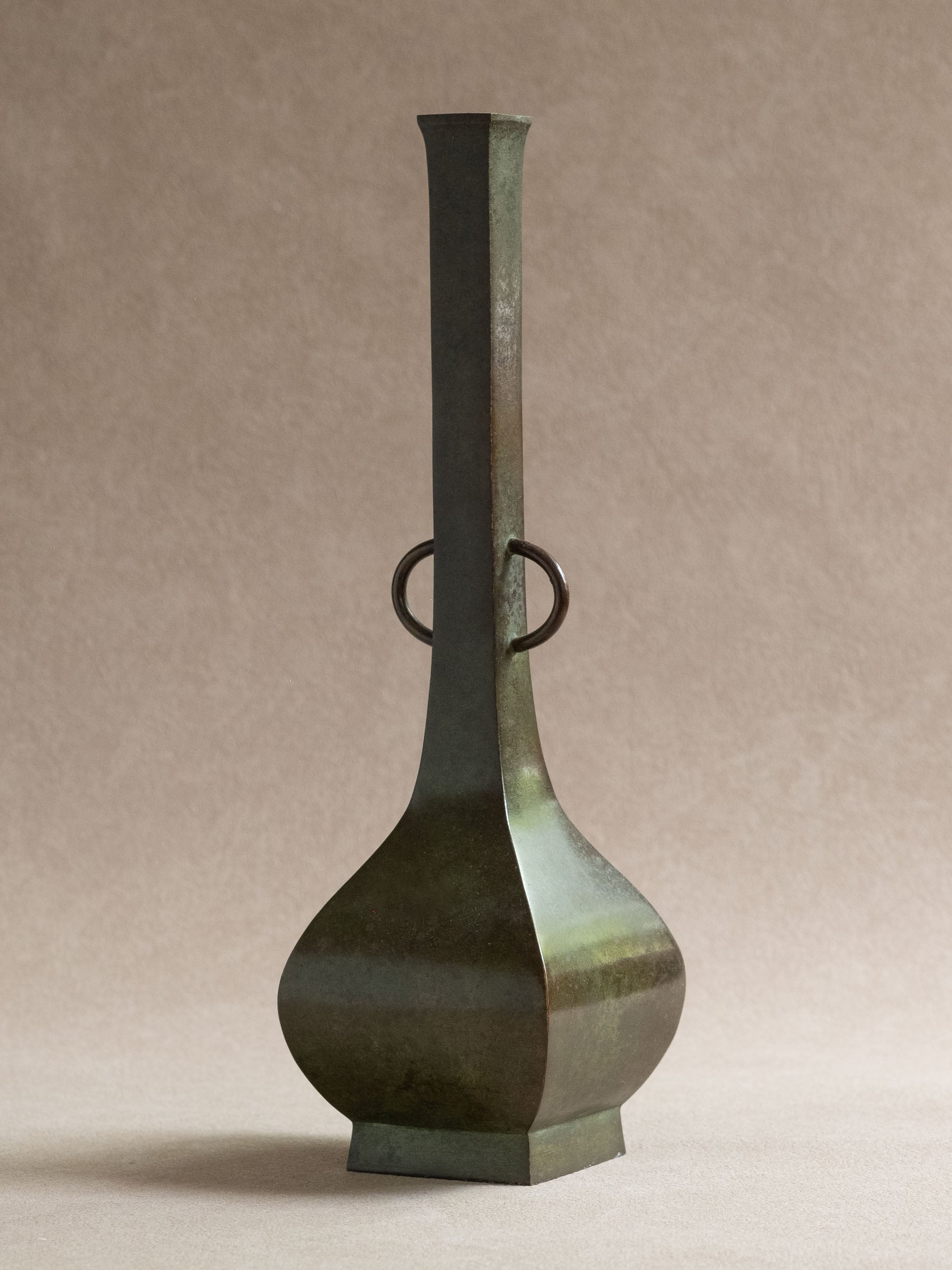 Japanese copper-alloy hanaire vase with square neck, ring handles, photographed in front of a beige background.