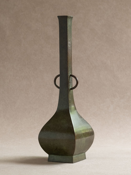 Japanese copper-alloy hanaire vase with square neck, ring handles, photographed in front of a beige background.