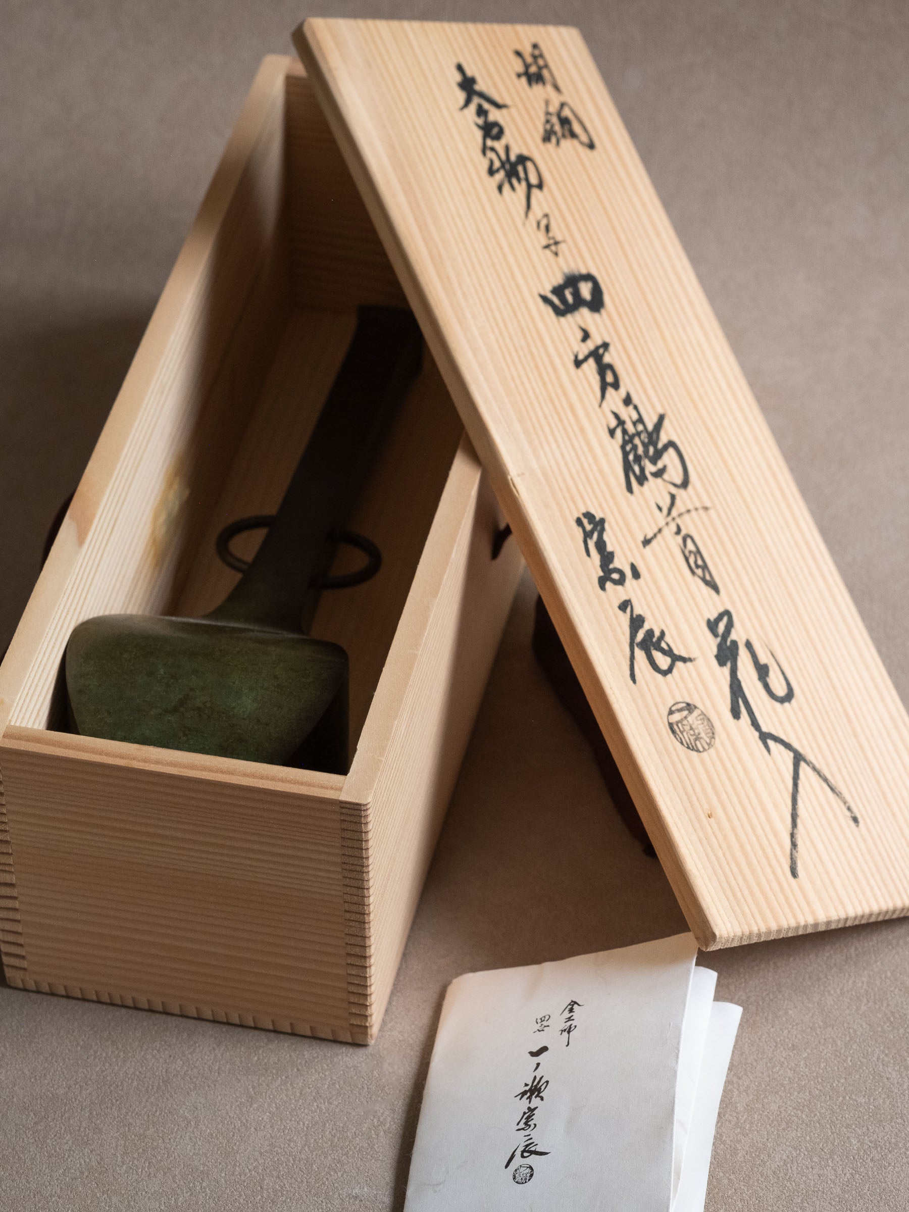Japanese copper-alloy hanaire vase shown inside its original inscribed wooden box and paper leaflet.
