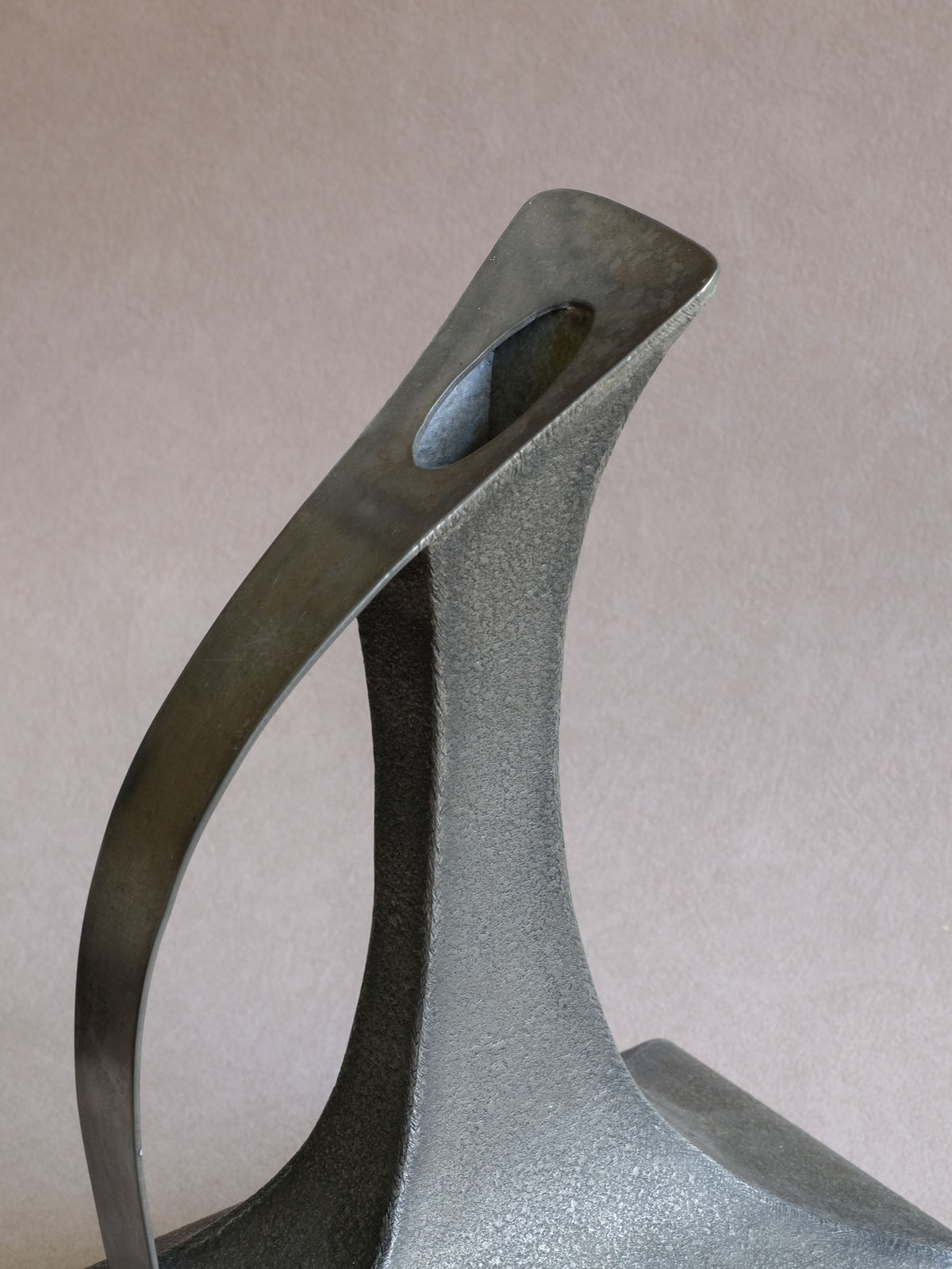 Close-up of curved handle and open spout on the tall Italian pewter decanter-form vase.