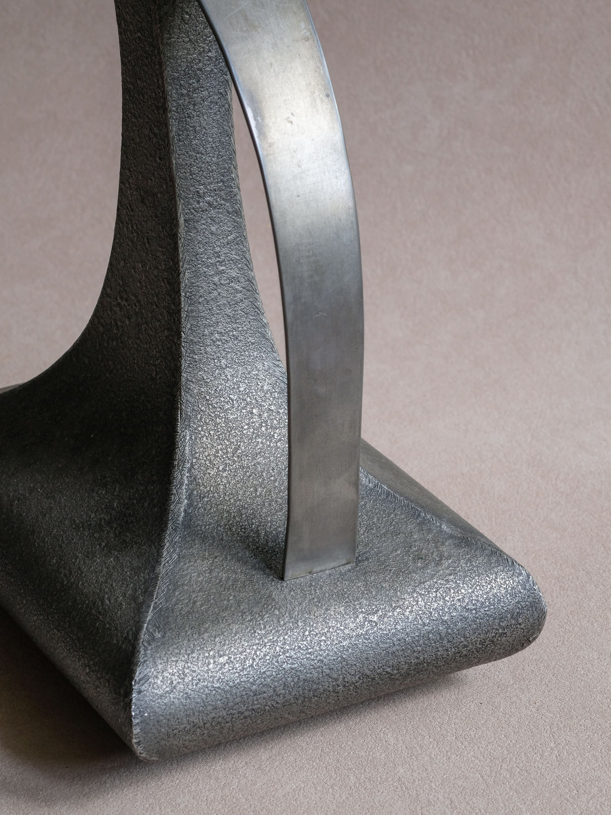 Detail of the curved handle joining the broad lower body of the Italian pewter decanter-form vase.