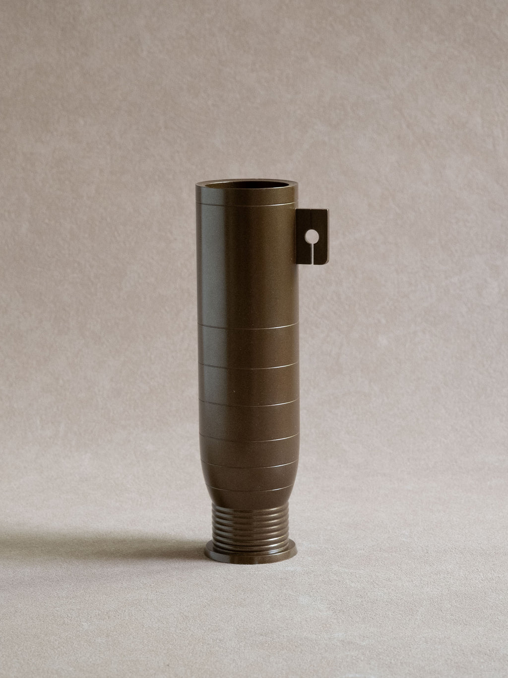 Full view of a Japanese brass flower vase with cylindrical body, side tab, and ribbed foot.
