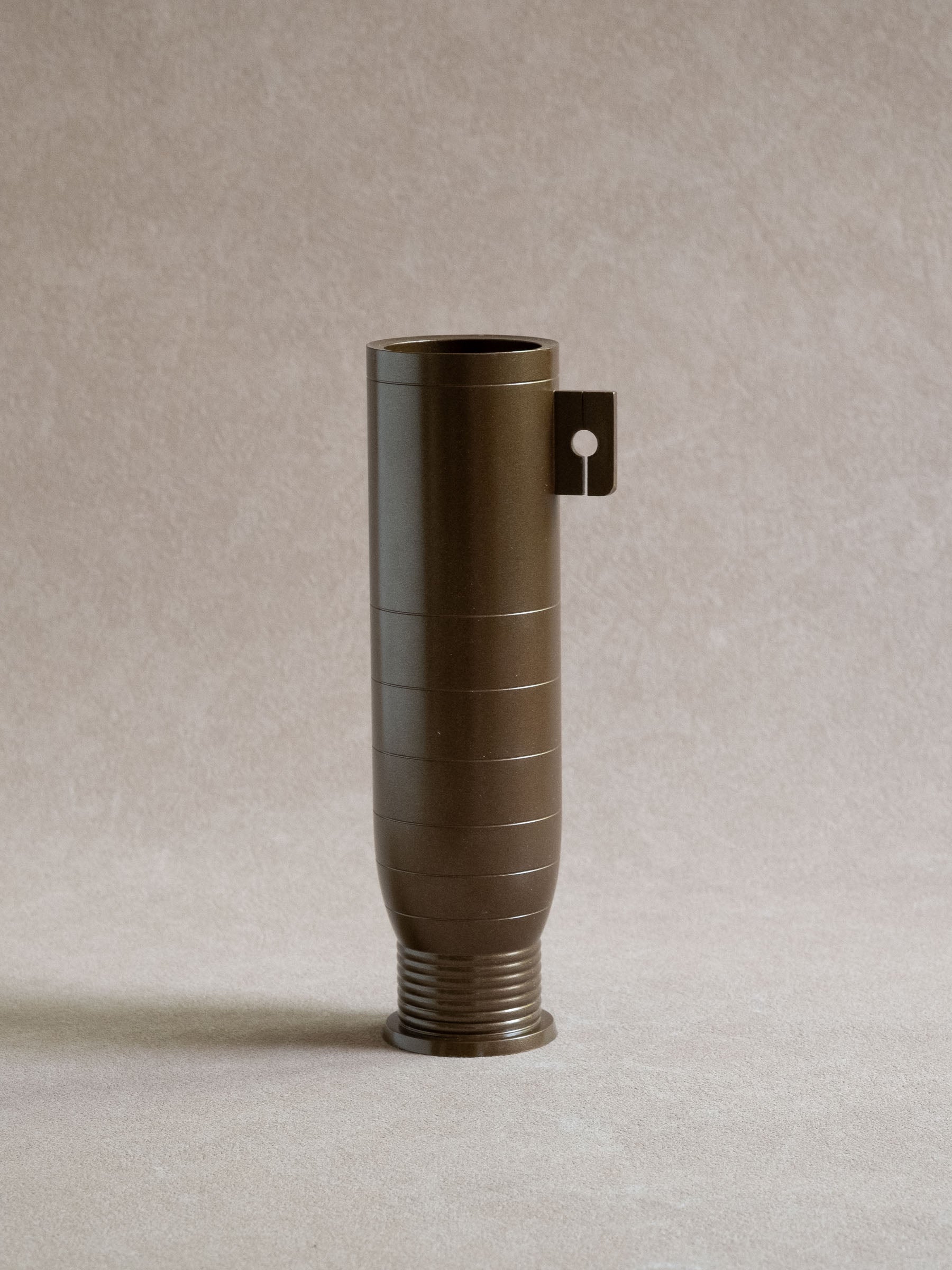 Full view of a Japanese brass flower vase with cylindrical body, side tab, and ribbed foot.

