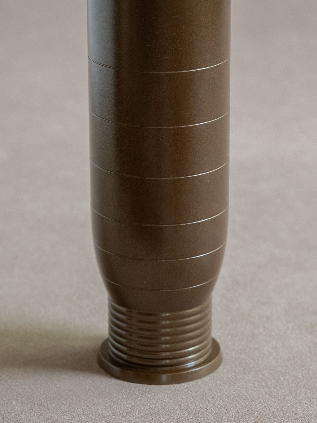 Close-up of the lower body and ribbed foot of a dark bronze-brown brass flower vase.
