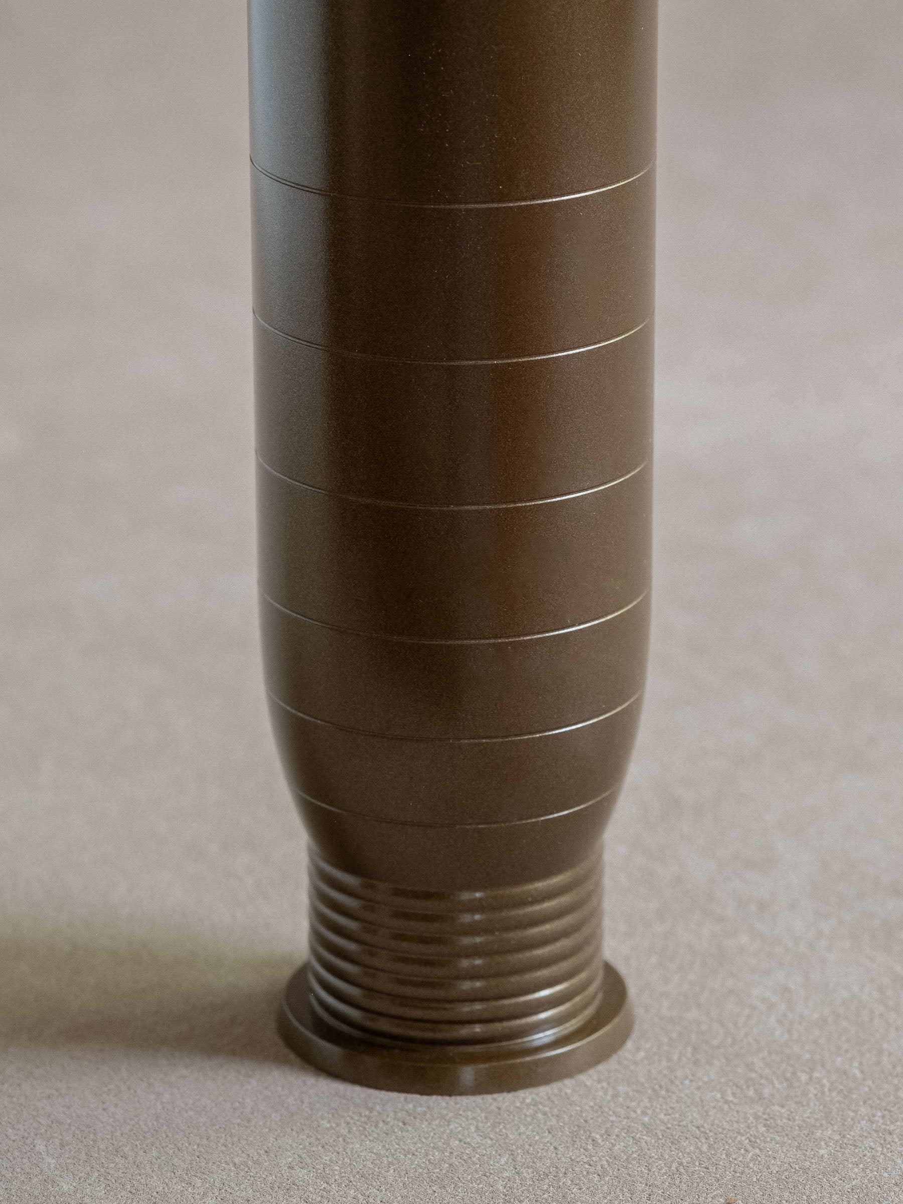 Close-up of the lower body and ribbed foot of a dark bronze-brown brass flower vase.
