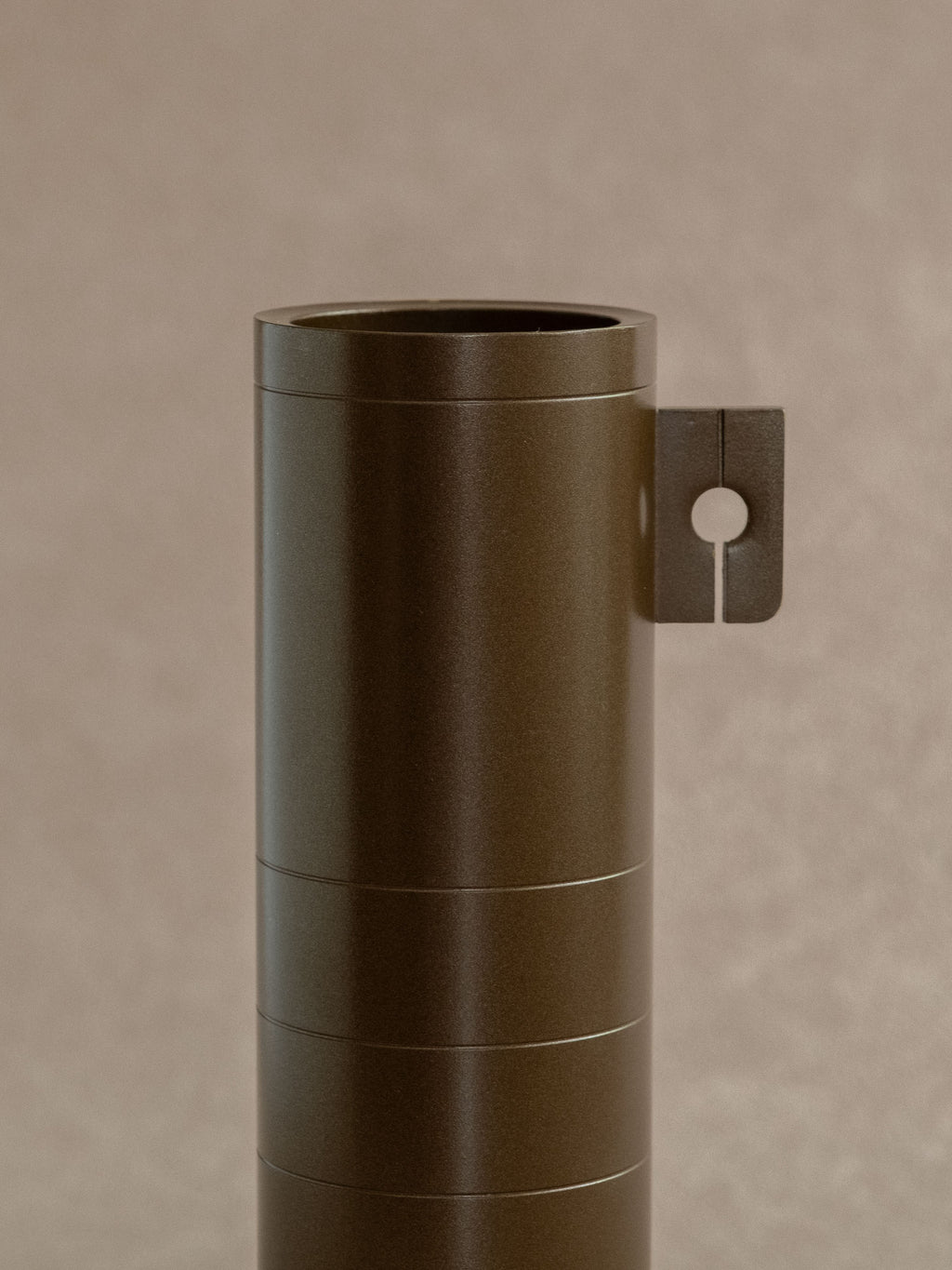 Close-up of a Japanese brass flower vase by Hasuda Shugoro showing the open rim and side tab with circular cut-out.
