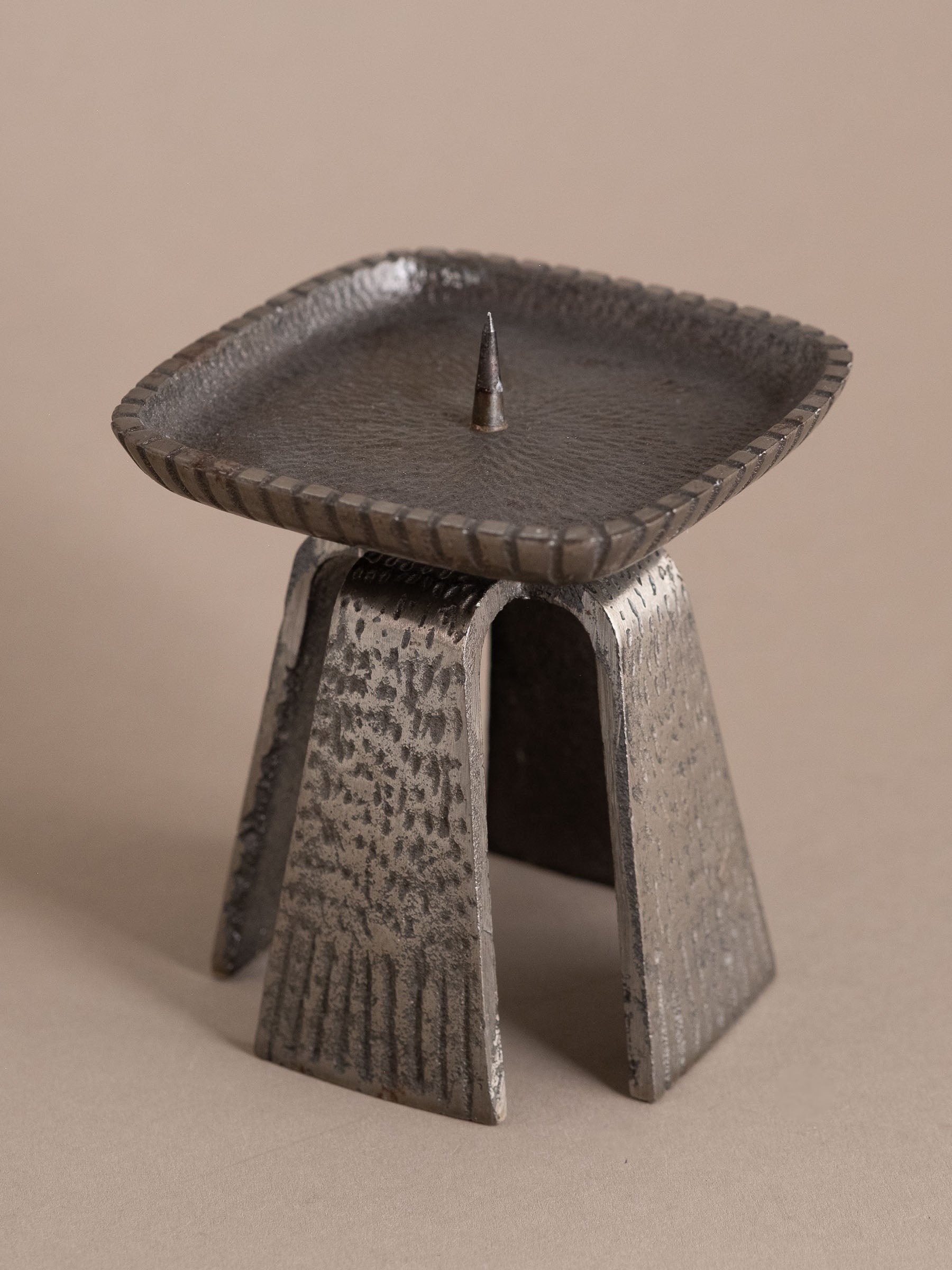 Japanese cast iron pricket candle holder shown at an angle, highlighting the square tray, central spike, and arched leg structure.