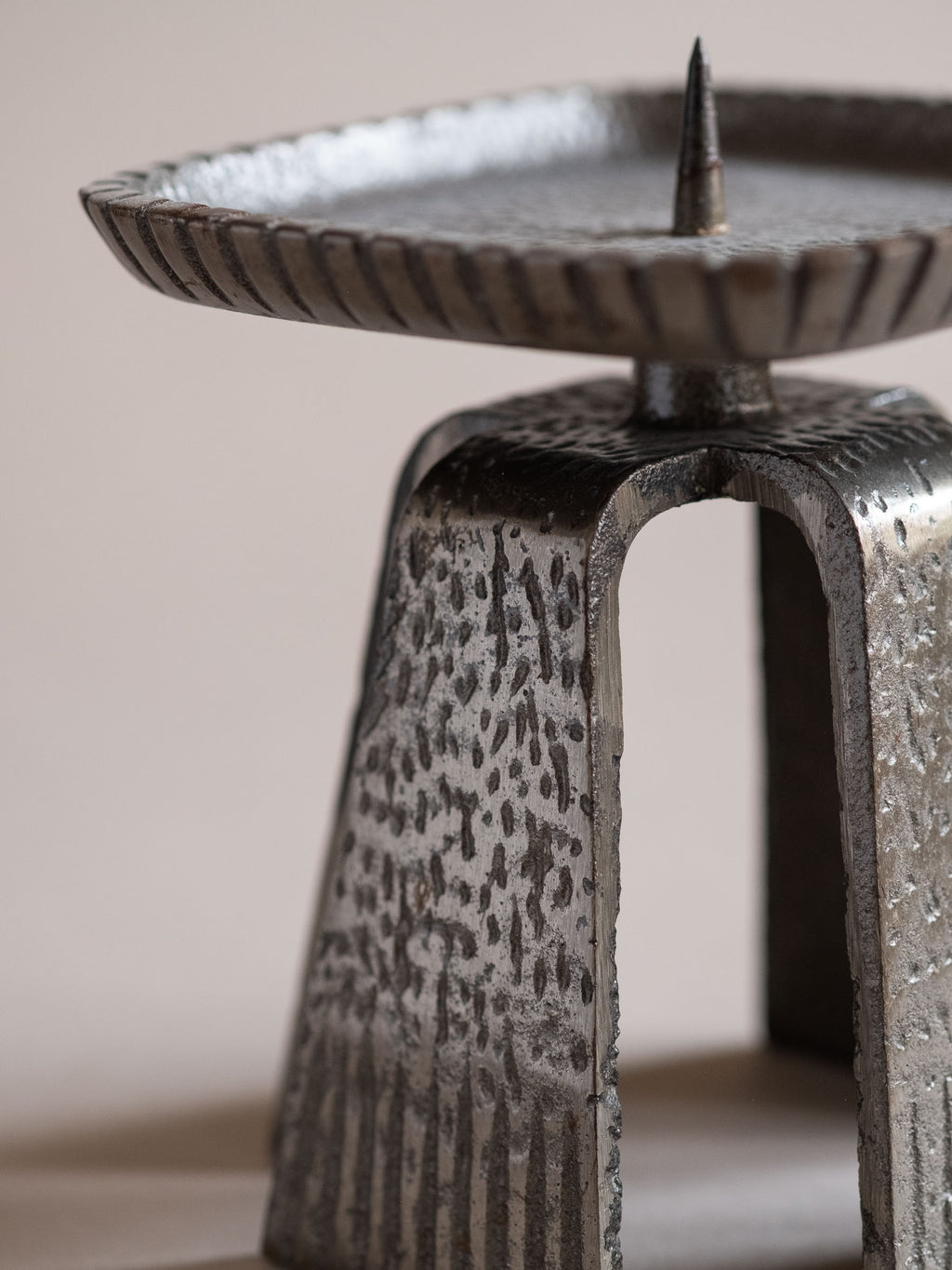 Close-up of the cast iron pricket candle holder with textured tapered legs and square drip tray.