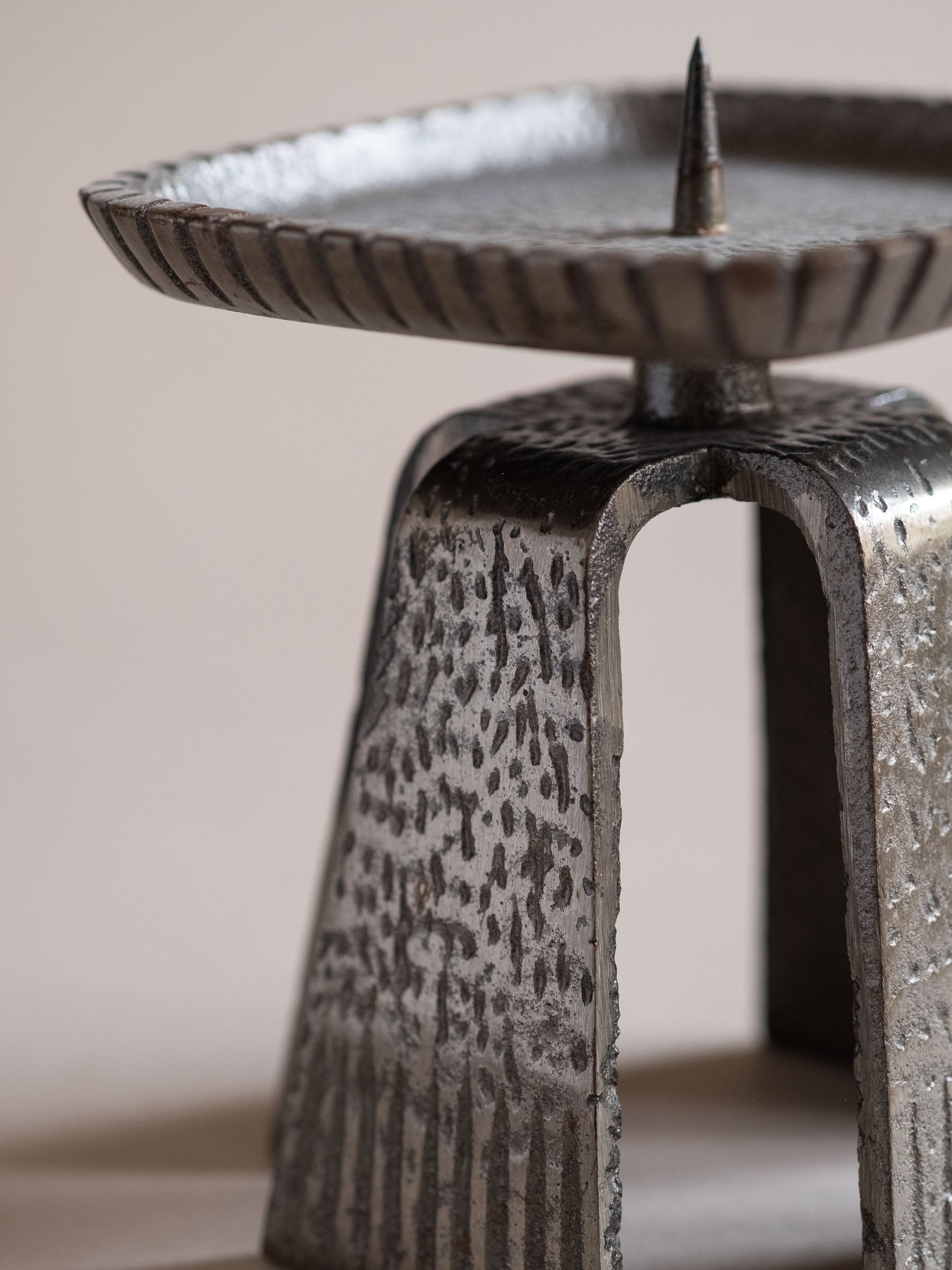 Close-up of the cast iron pricket candle holder with textured tapered legs and square drip tray.