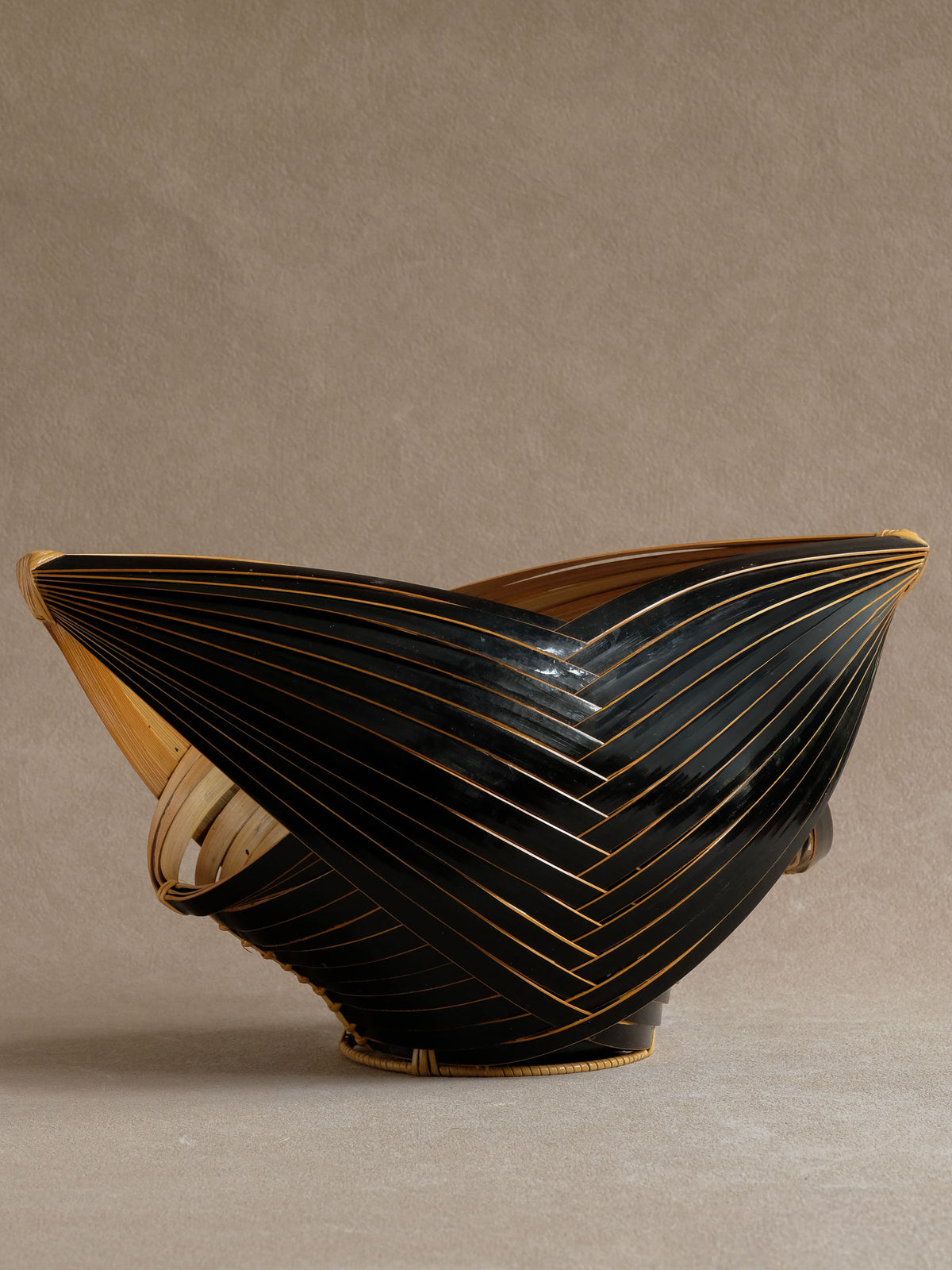 Full view of Japanese dark bamboo flower basket, with overlapping black strips and pale bamboo edges.