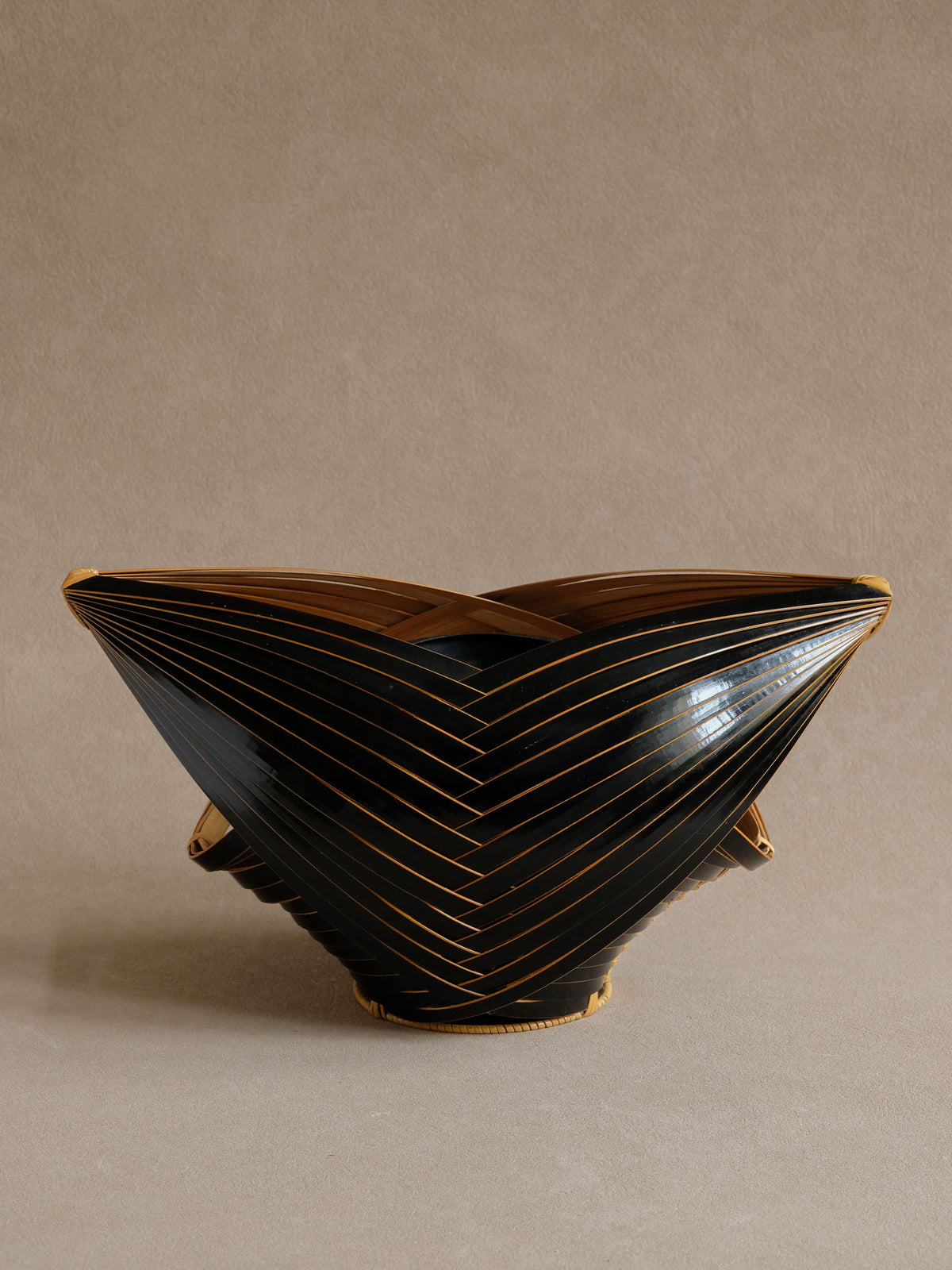 Side silhouette of angular dark bamboo ikebana basket on a neutral background.