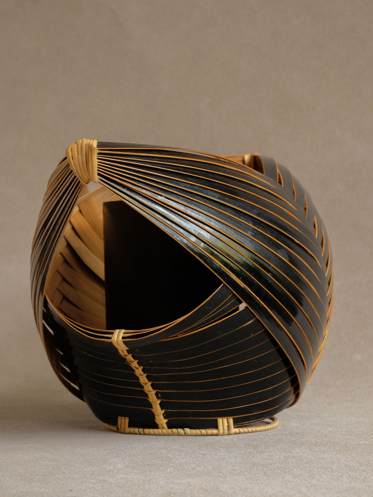 Three-quarter view of sculptural dark Japanese bamboo basket showing the curving layered body.