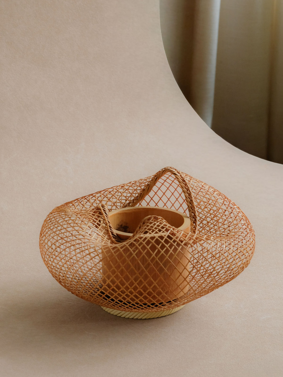 Light bamboo ikebana flower basket photographed in a quiet interior setting.
