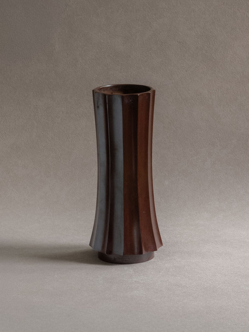 Front view of a tall Japanese Takaoka cast copper vase with faceted body, open mouth, and dark patina.
