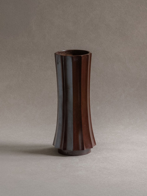 Front view of a tall Japanese Takaoka cast copper vase with faceted body, open mouth, and dark patina.
