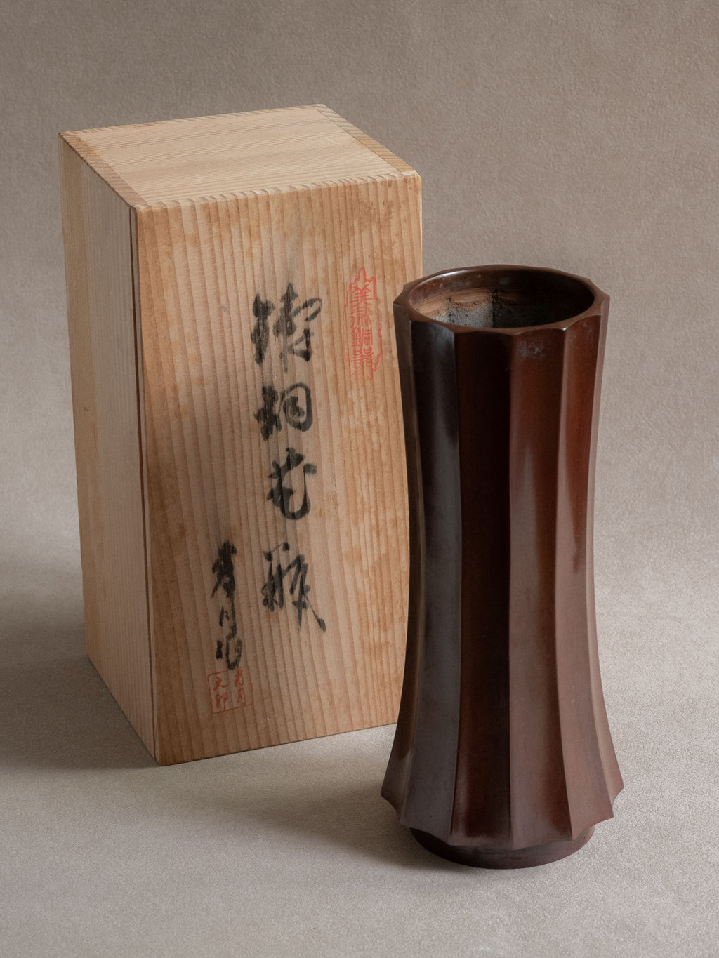 Japanese Takaoka cast copper faceted vase shown beside its original wooden storage box.

