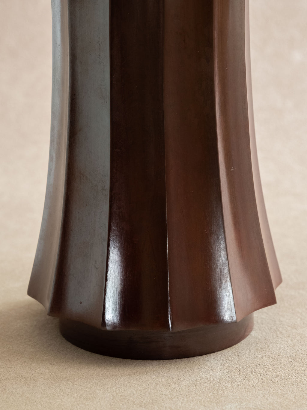 Close-up of the lower faceted body of a dark reddish-brown Takaoka cast copper vase.
