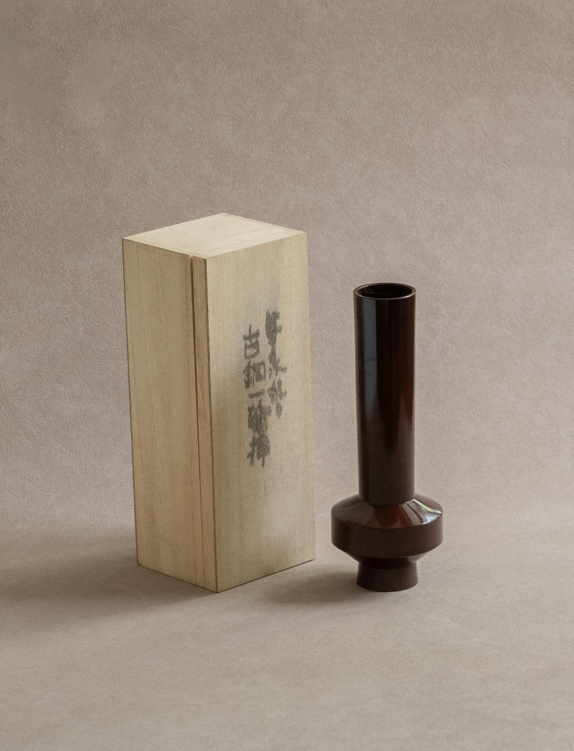 Japanese Takaoka copperware single-flower vase with dark reddish-brown patina, shown beside its original wooden storage box.
