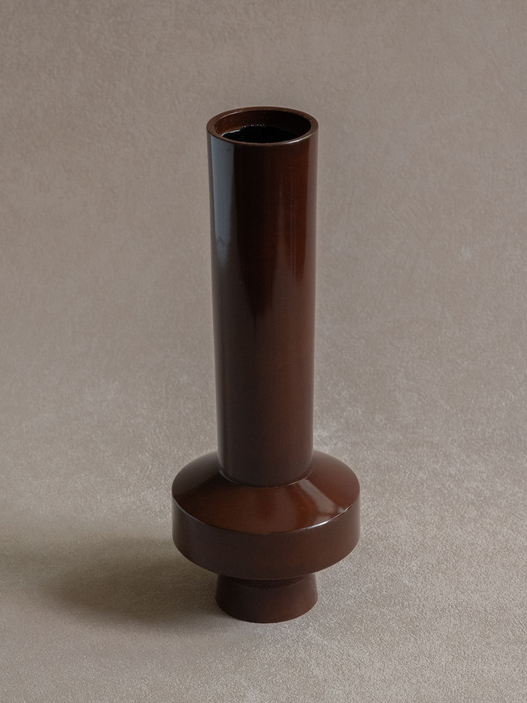Close-up view of a Japanese copper-alloy single-flower vase with tall cylindrical neck, narrow mouth, and stepped circular base.
