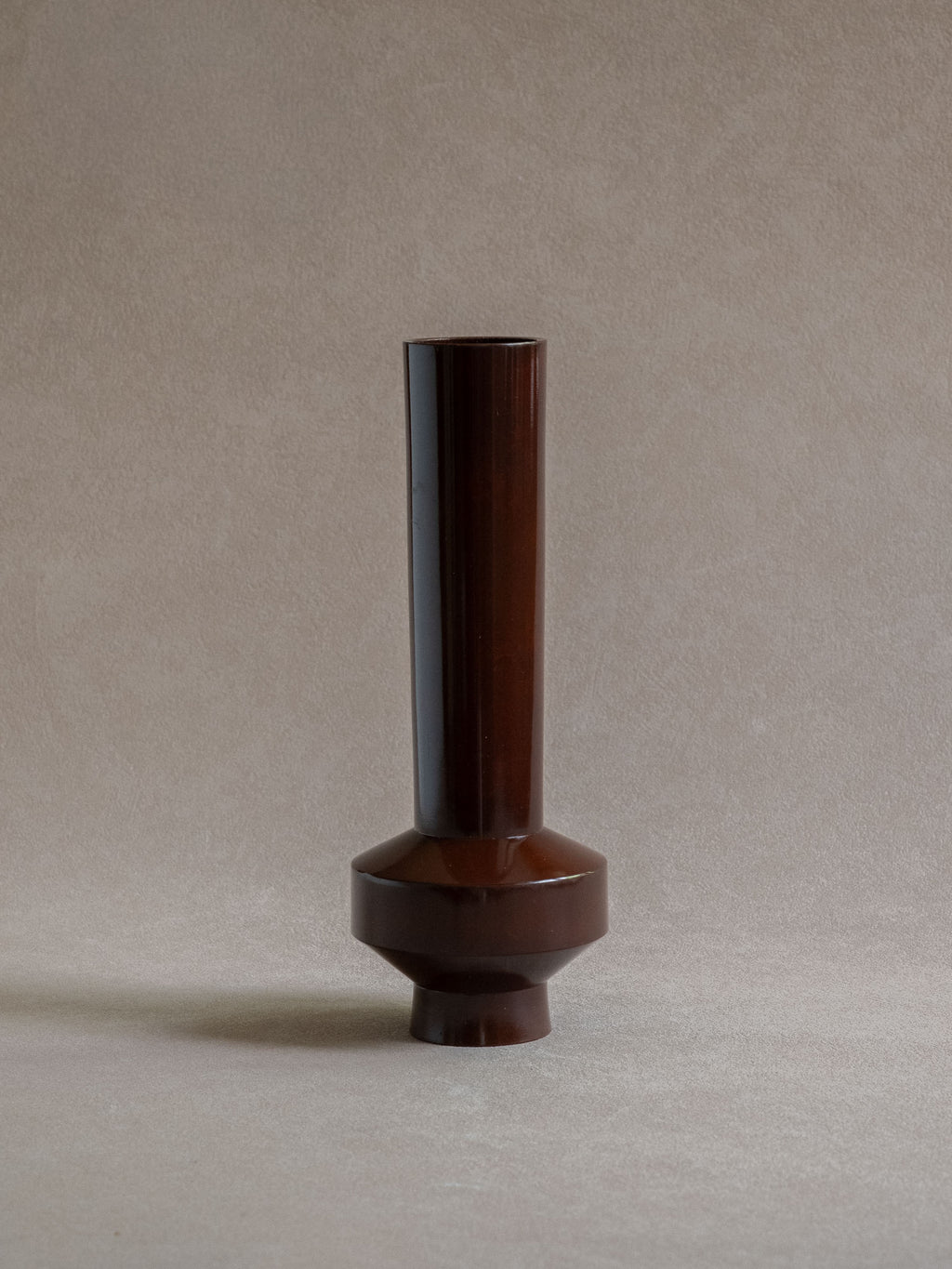Full view of a Japanese patinated copper-alloy single-flower vase with tall narrow form and raised circular base.
