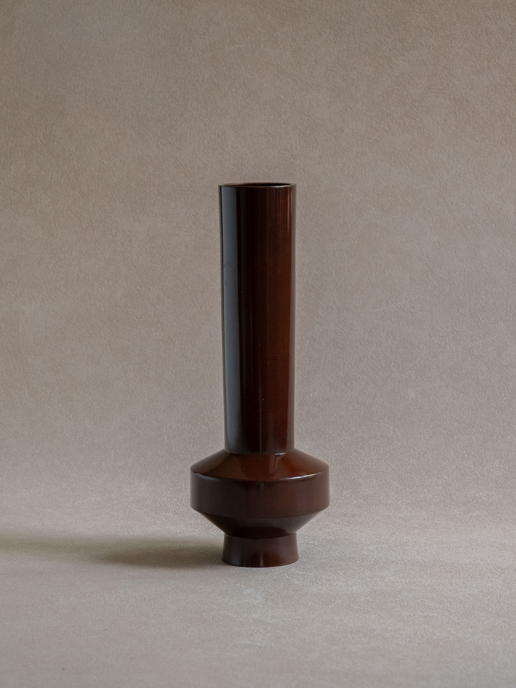 Full view of a Japanese patinated copper-alloy single-flower vase with tall narrow form and raised circular base.

