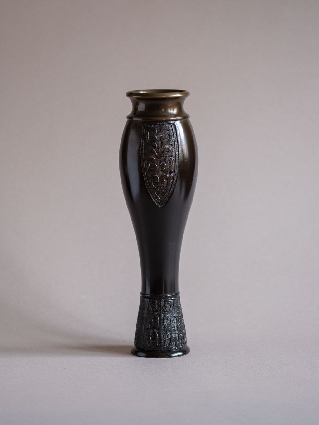 Studio view of a Japanese bronze flower vase by Kanamori Shōei showing its full form against a pale background.