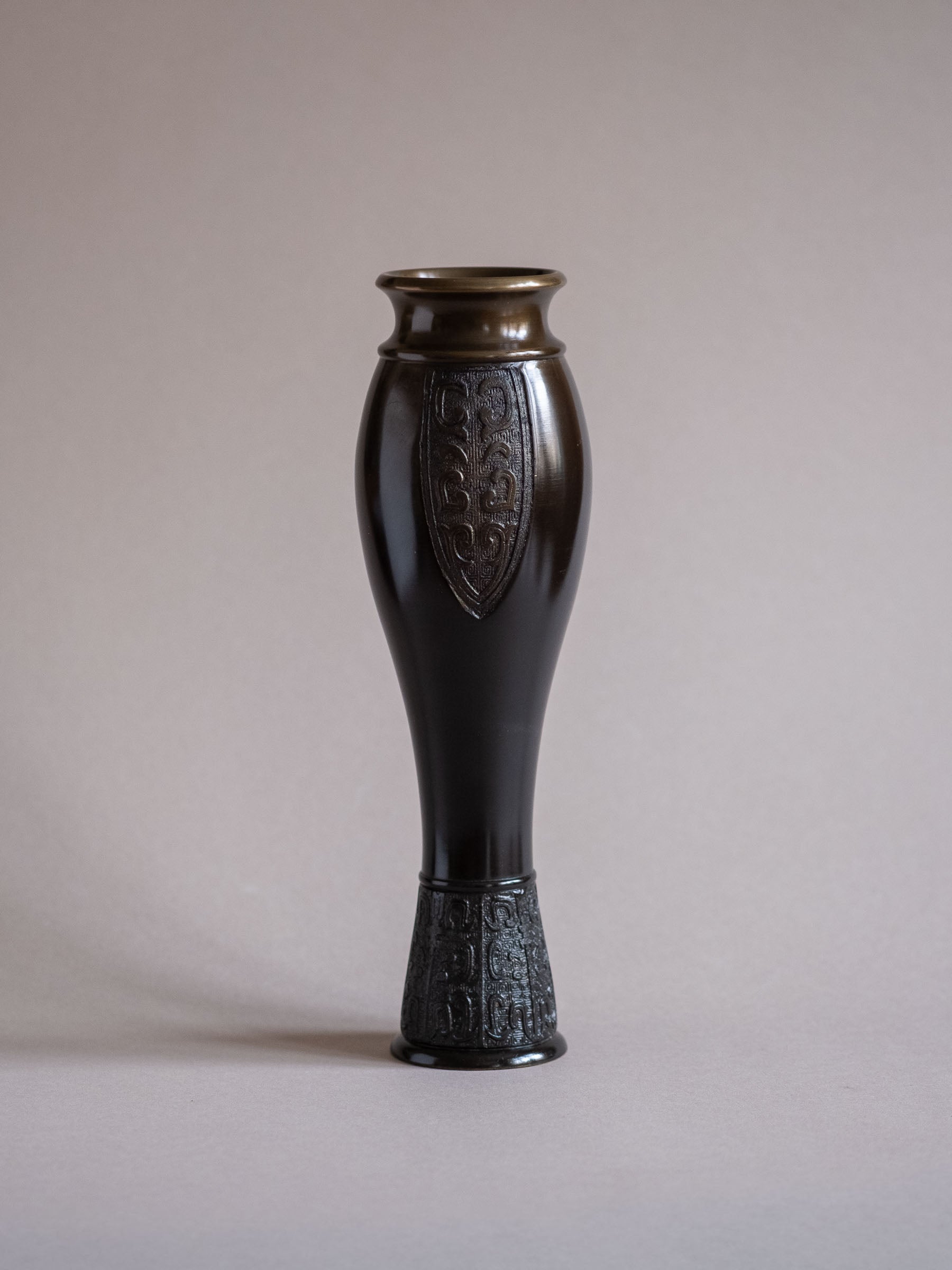 Studio view of a Japanese bronze flower vase by Kanamori Shōei showing its full form against a pale background.