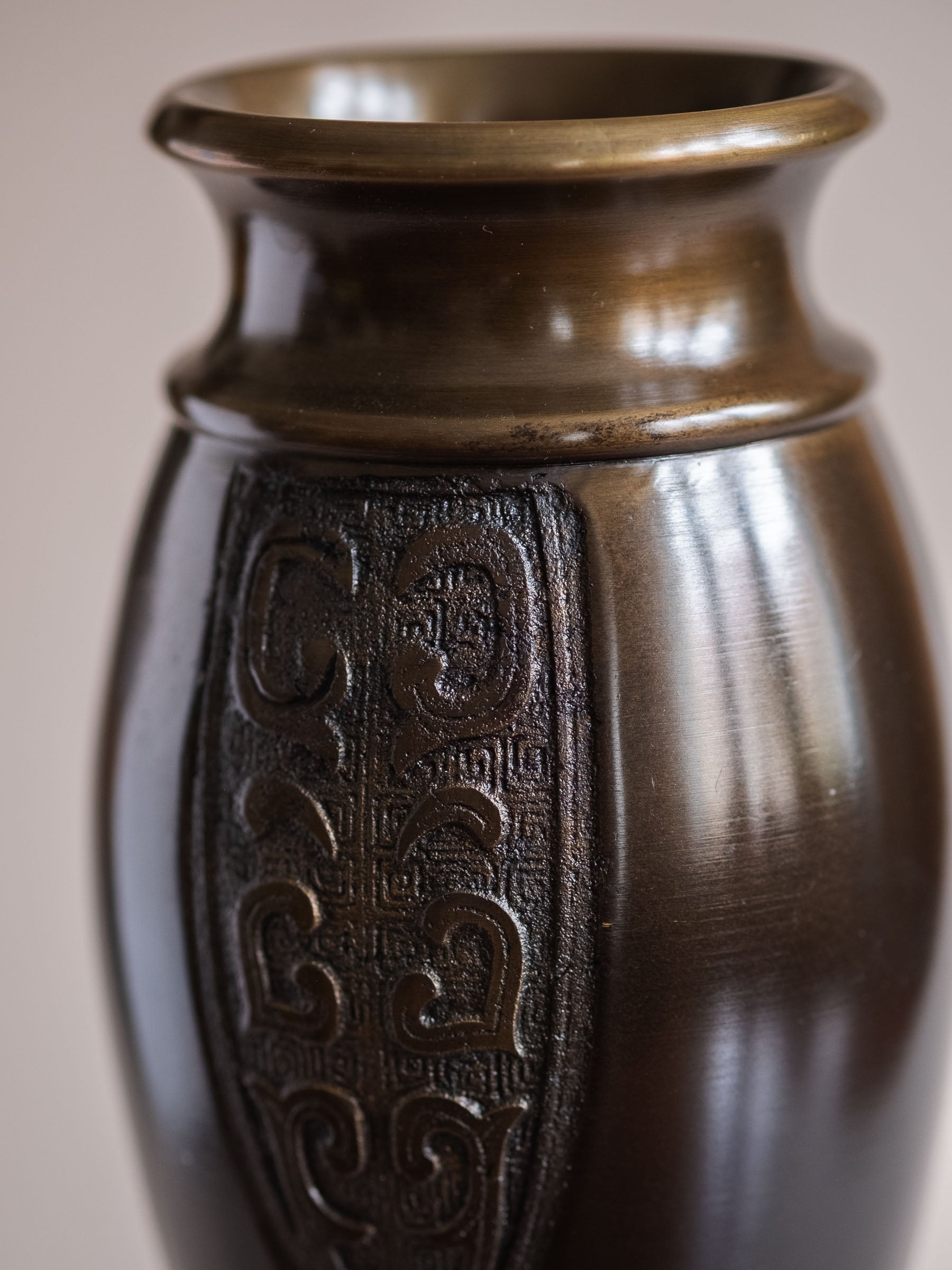 Close-up of the upper body and rim of a Japanese bronze flower vase showing the relief panel and bronze-toned surface.