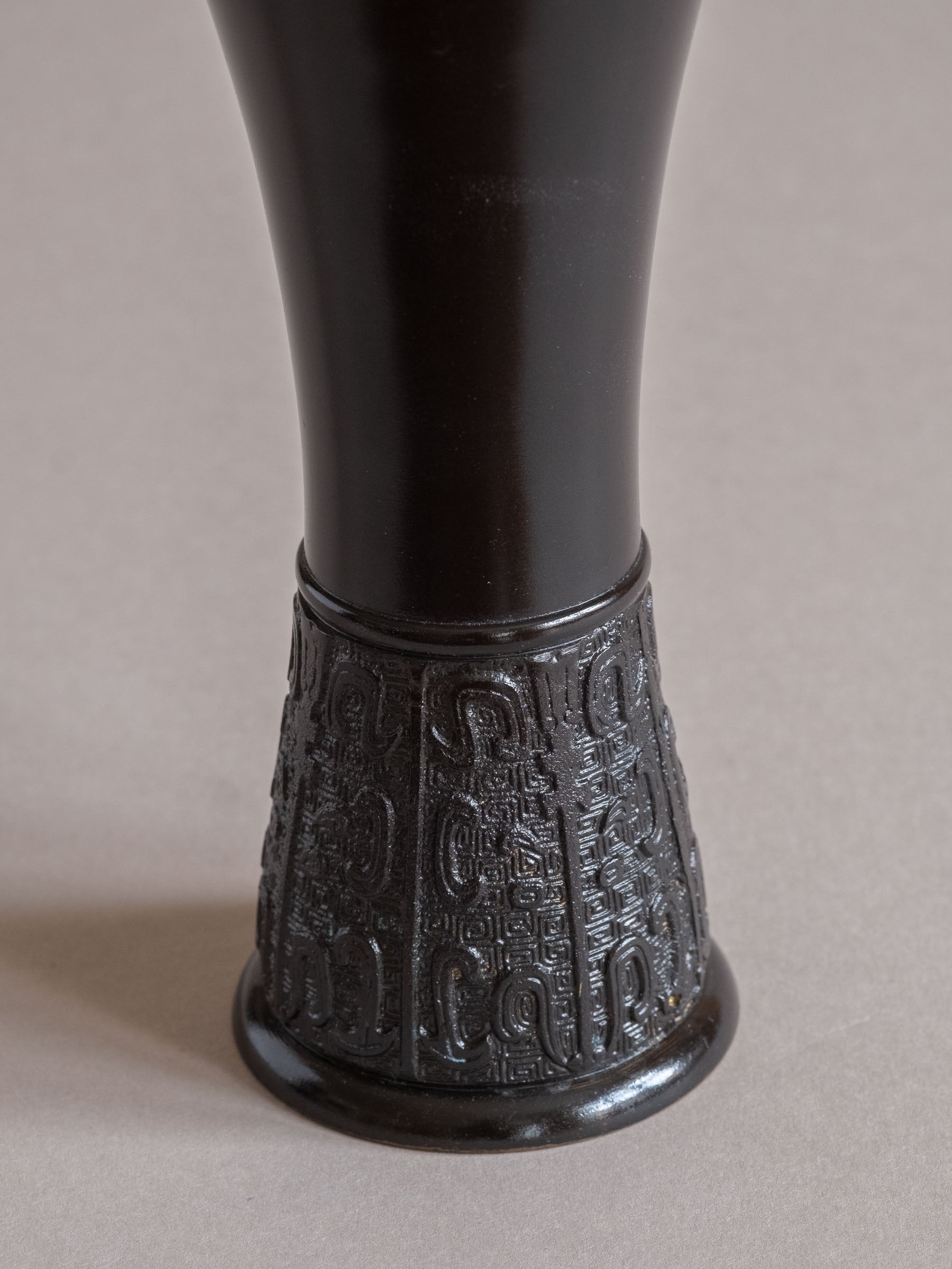 Close-up of the lower section of a Japanese bronze flower vase with dark patina and cast relief pattern around the foot.