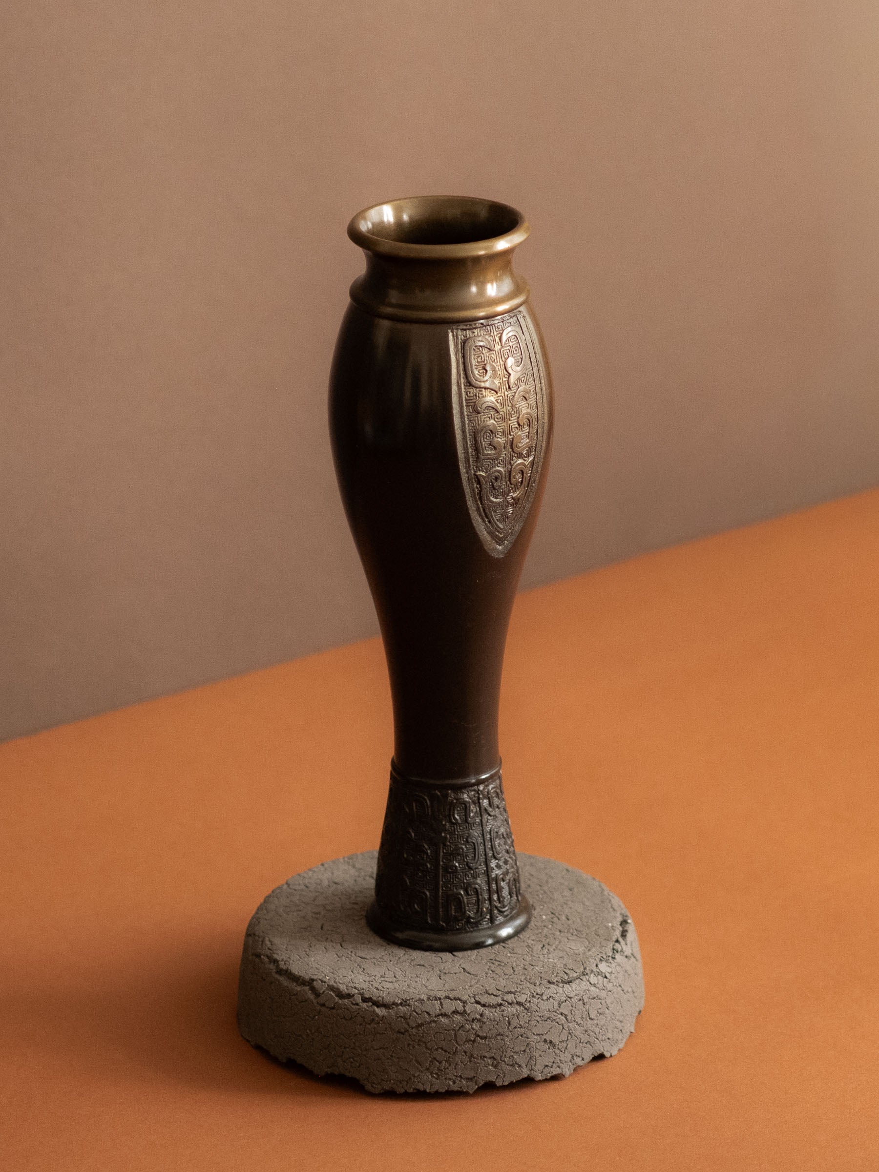 Three-quarter view of a Japanese bronze flower vase by Kanamori Shōei with rolled rim, dark patina, and cast relief decoration.
