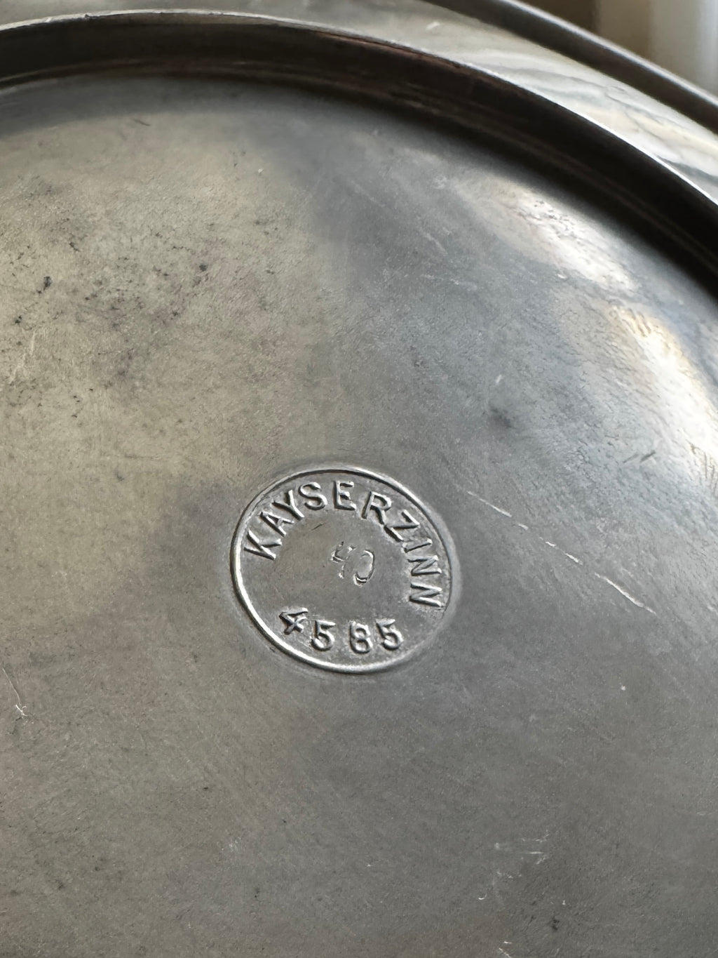 Close-up of the underside stamp on a Kayserzinn pewter bowl showing circular “KAYSERZINN 40 4585” maker’s mark impressed into the metal surface.