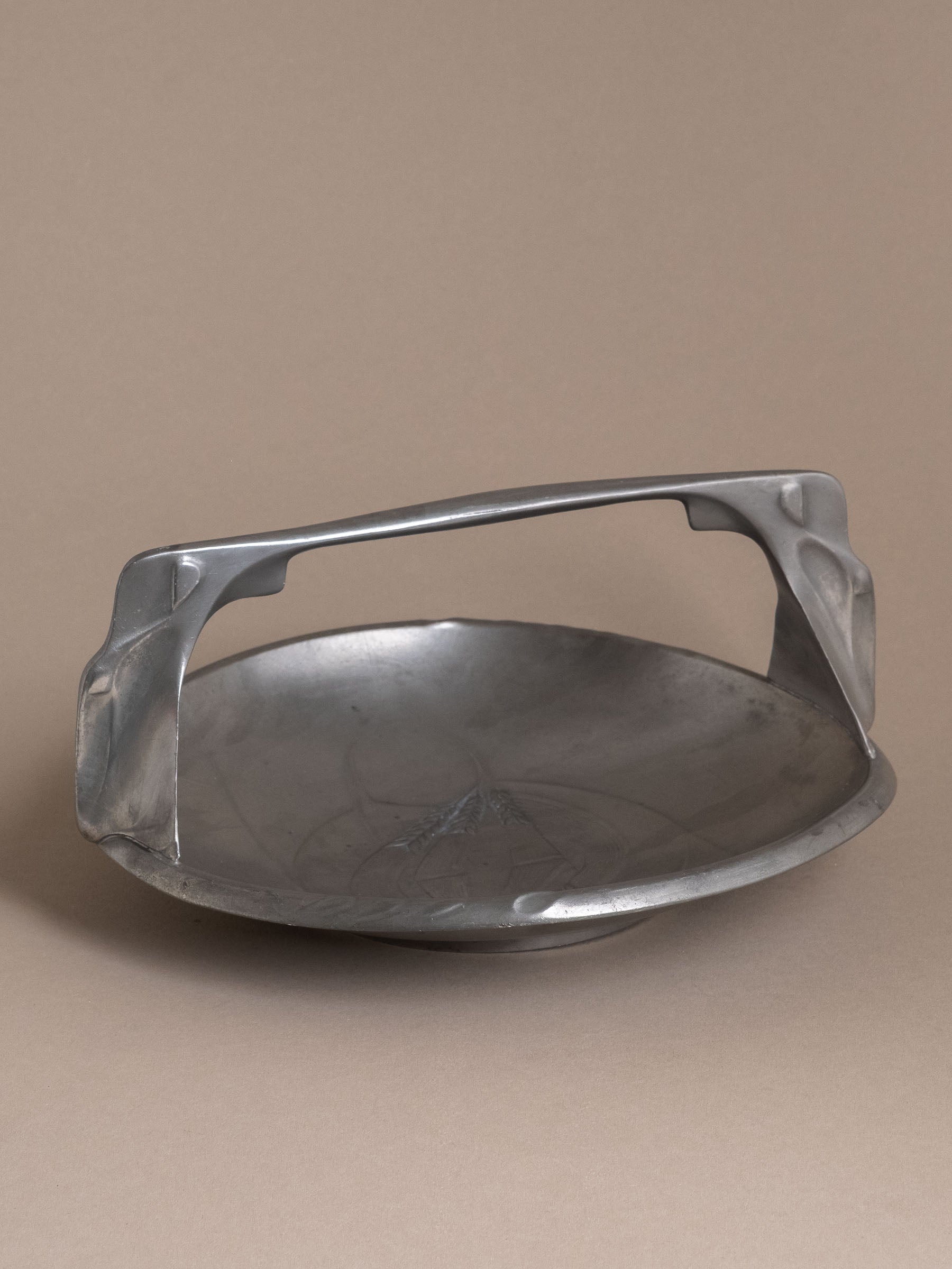 Kayserzinn pewter handled bowl with arched integrated handle and shallow circular basin, photographed against a neutral brown background.