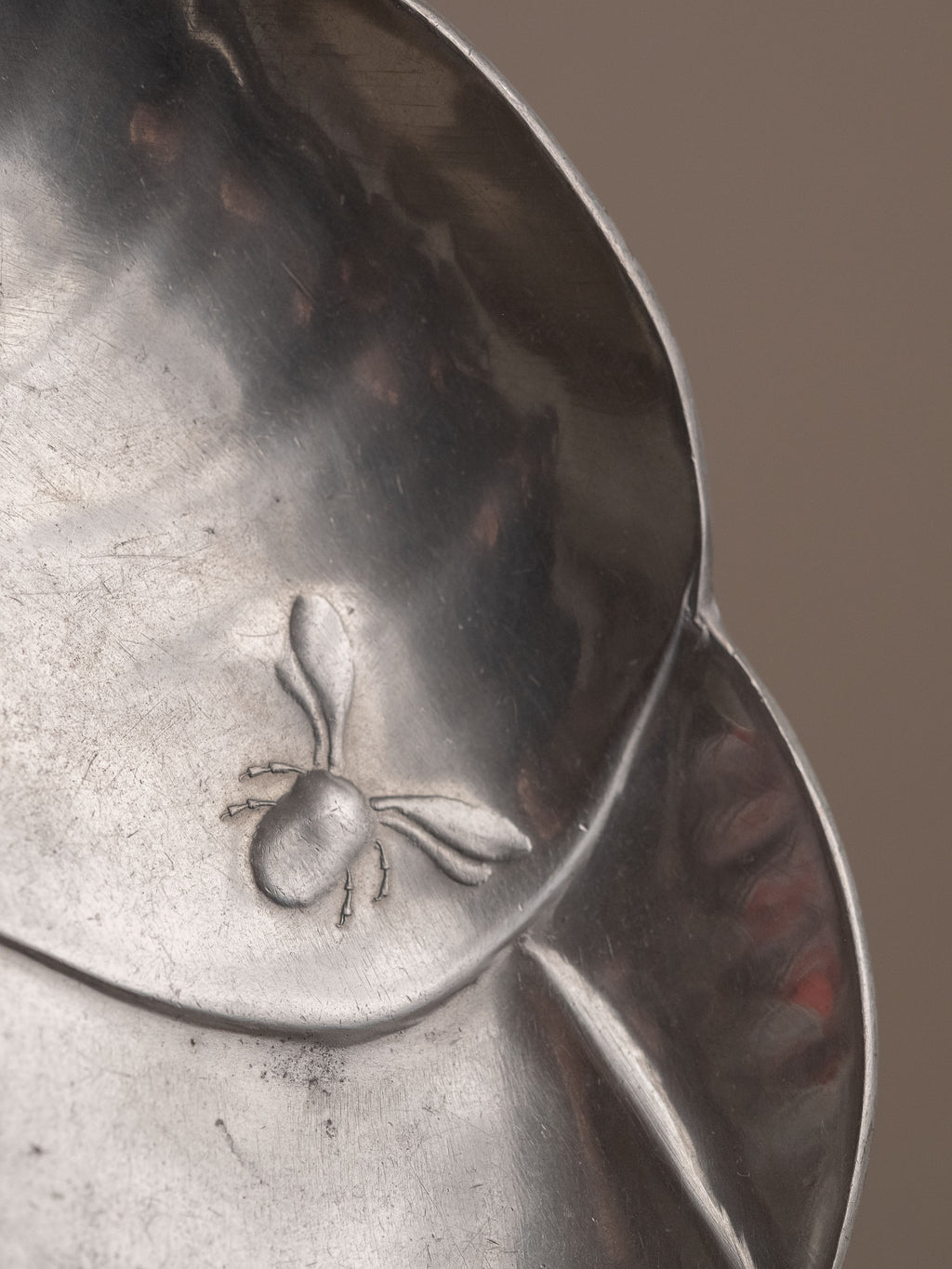 Close-up of a small insect relief on the pewter dish, showing surface wear and fine incised detail.