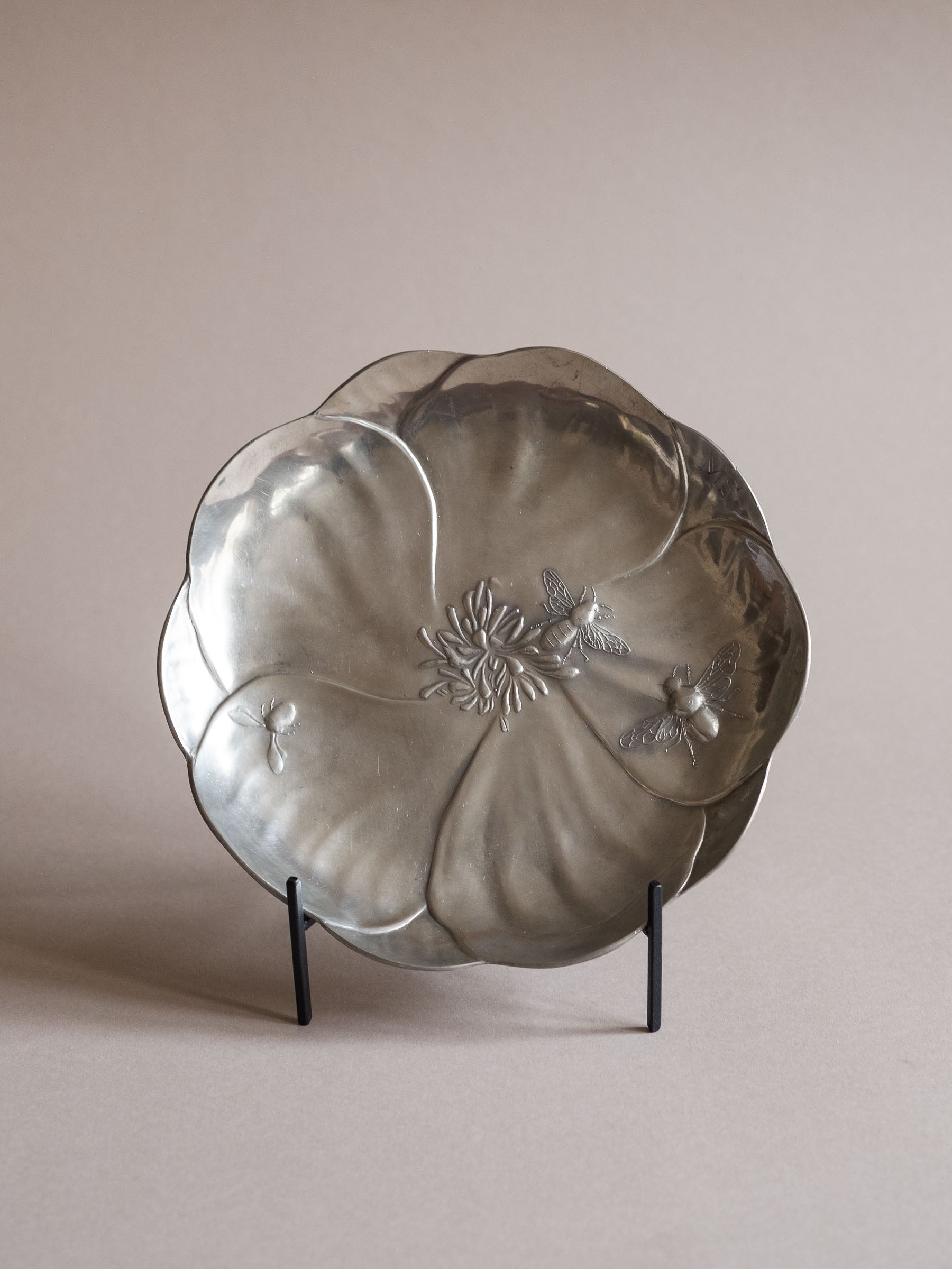 Front-facing view of the Kayserzinn pewter dish on a stand, showing the open flower form and central floral relief.
