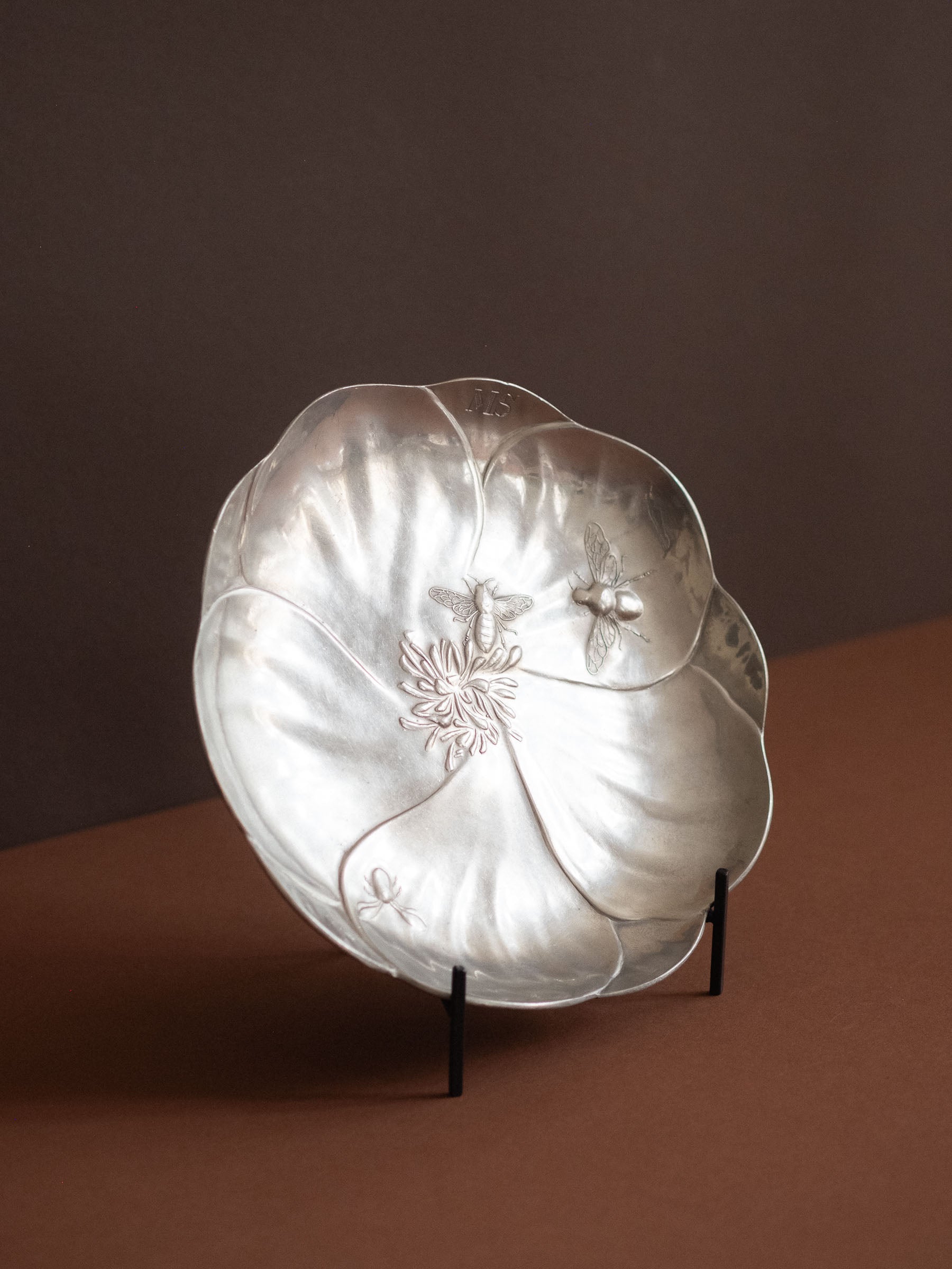 Kayserzinn pewter bee dish shown upright against a brown background, highlighting the curved petal rim and shallow form.