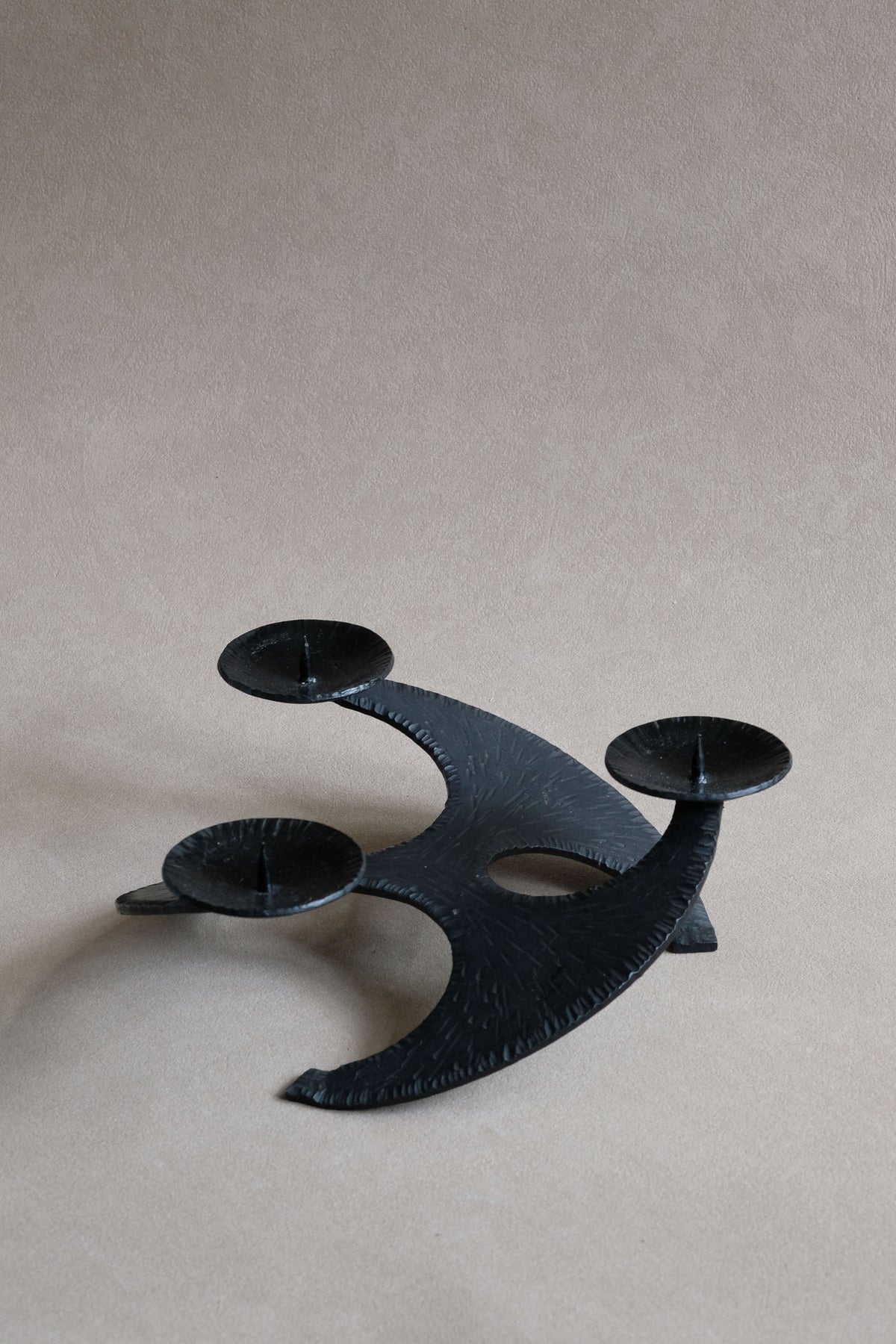 Large Brutalist cast iron three-arm candleholder, angled full view showing curved body and negative space.